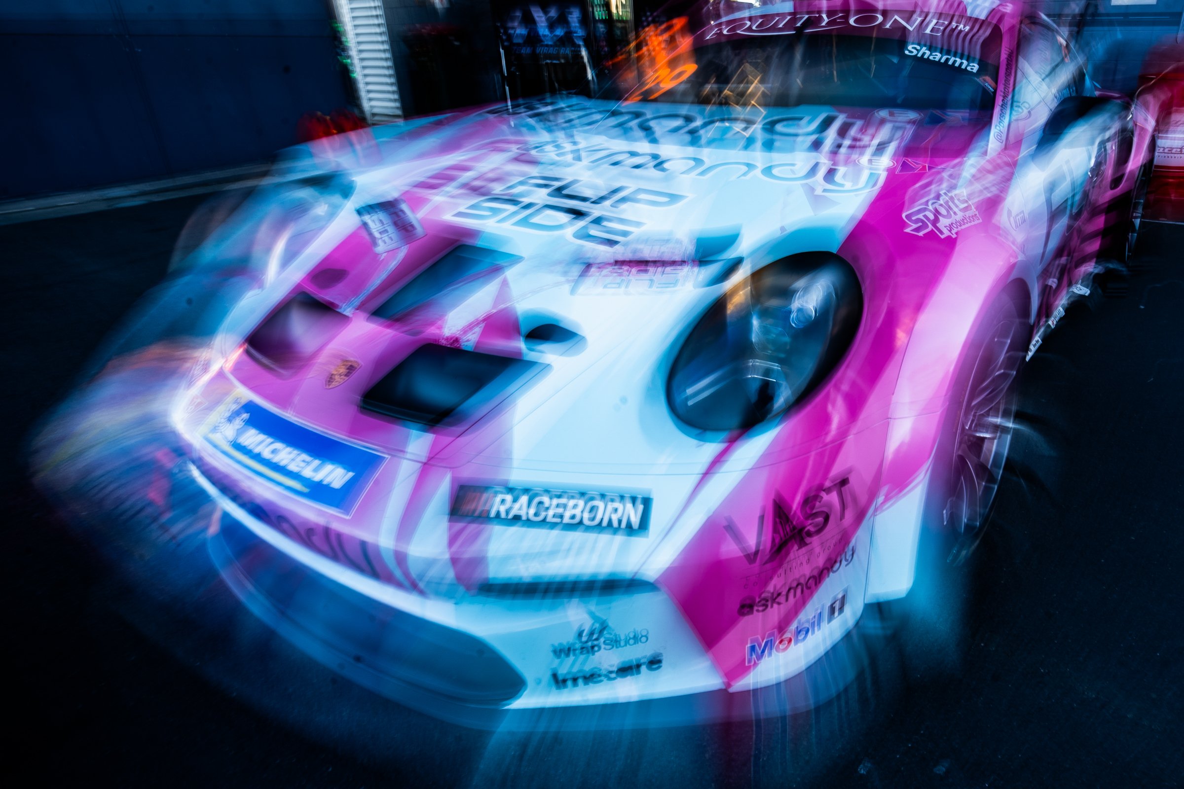 Pink and teal Porsche race car with sponsor logos captured with a motion blur effect