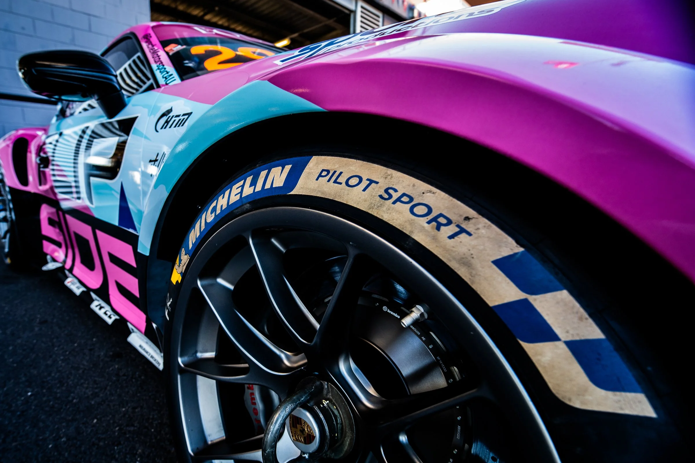 Close‑up of a pink and blue Porsche race car’s front right wheel showing Michelin Pilot Sport branding
