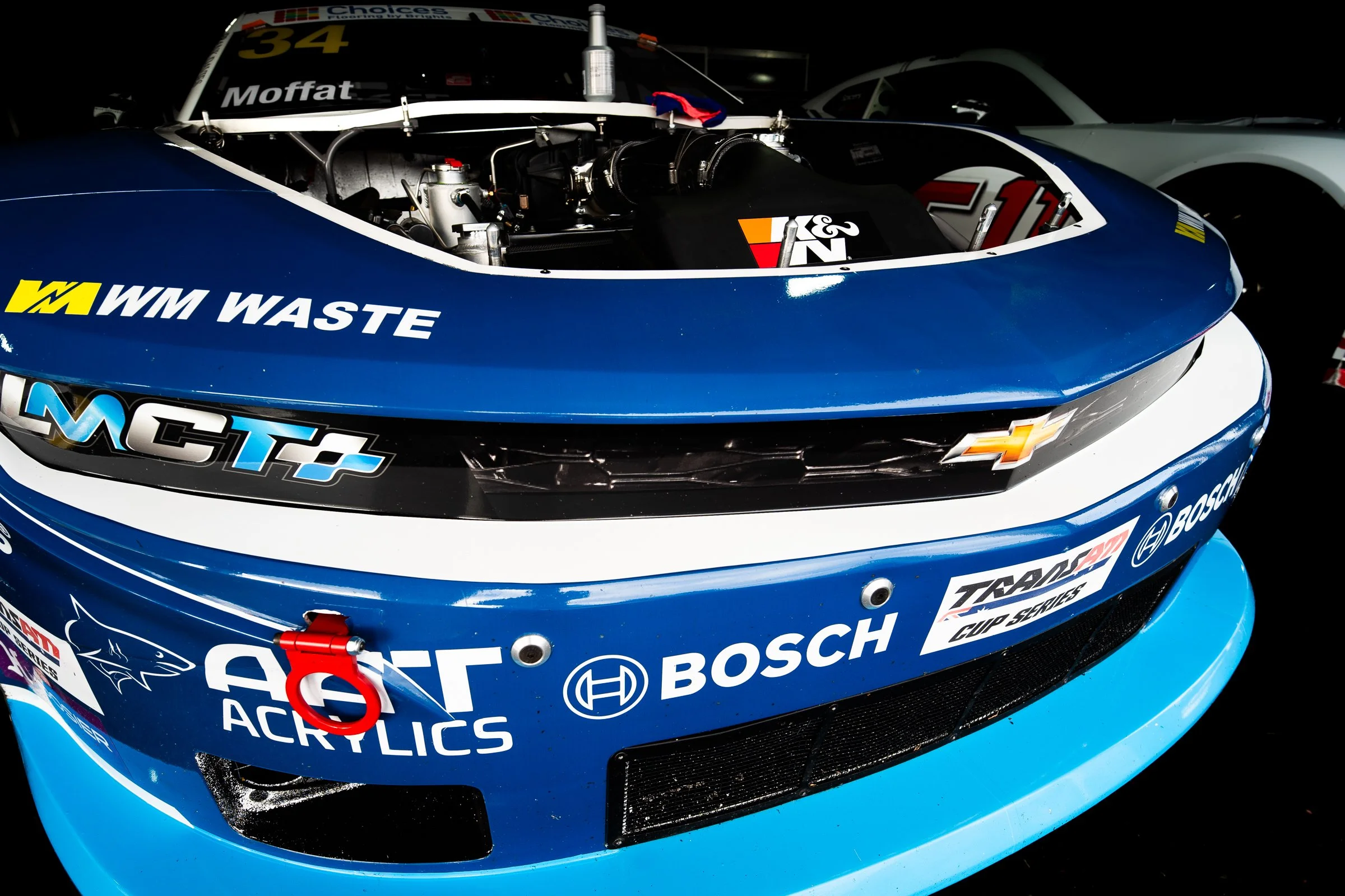 Close‑up of a blue race car front showing sponsor logos, a Chevrolet emblem and the engine visible through the hood opening
