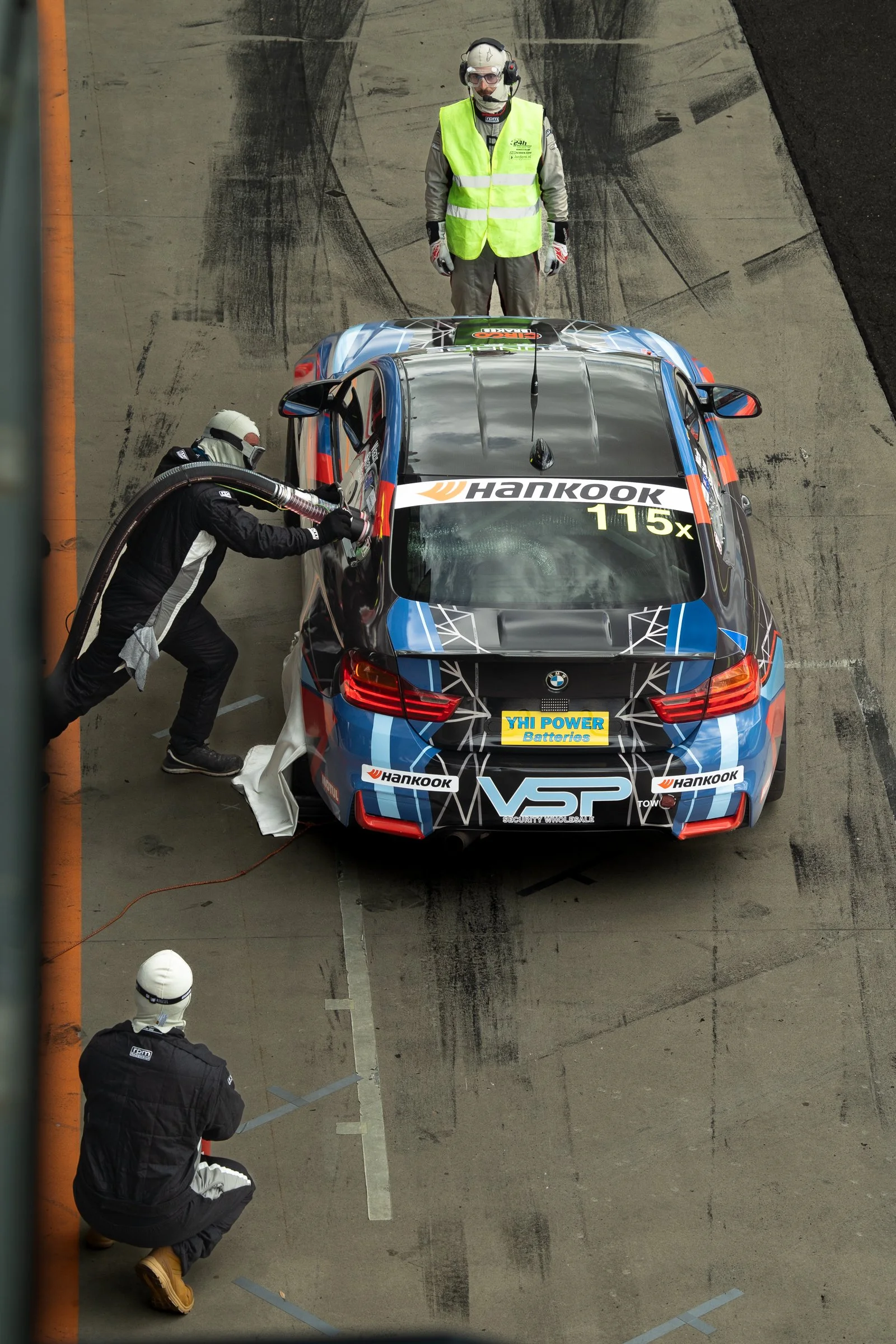 Aerial view of a race car being refuelled during a pit stop, surrounded by crew members in racing gear and safety equipment