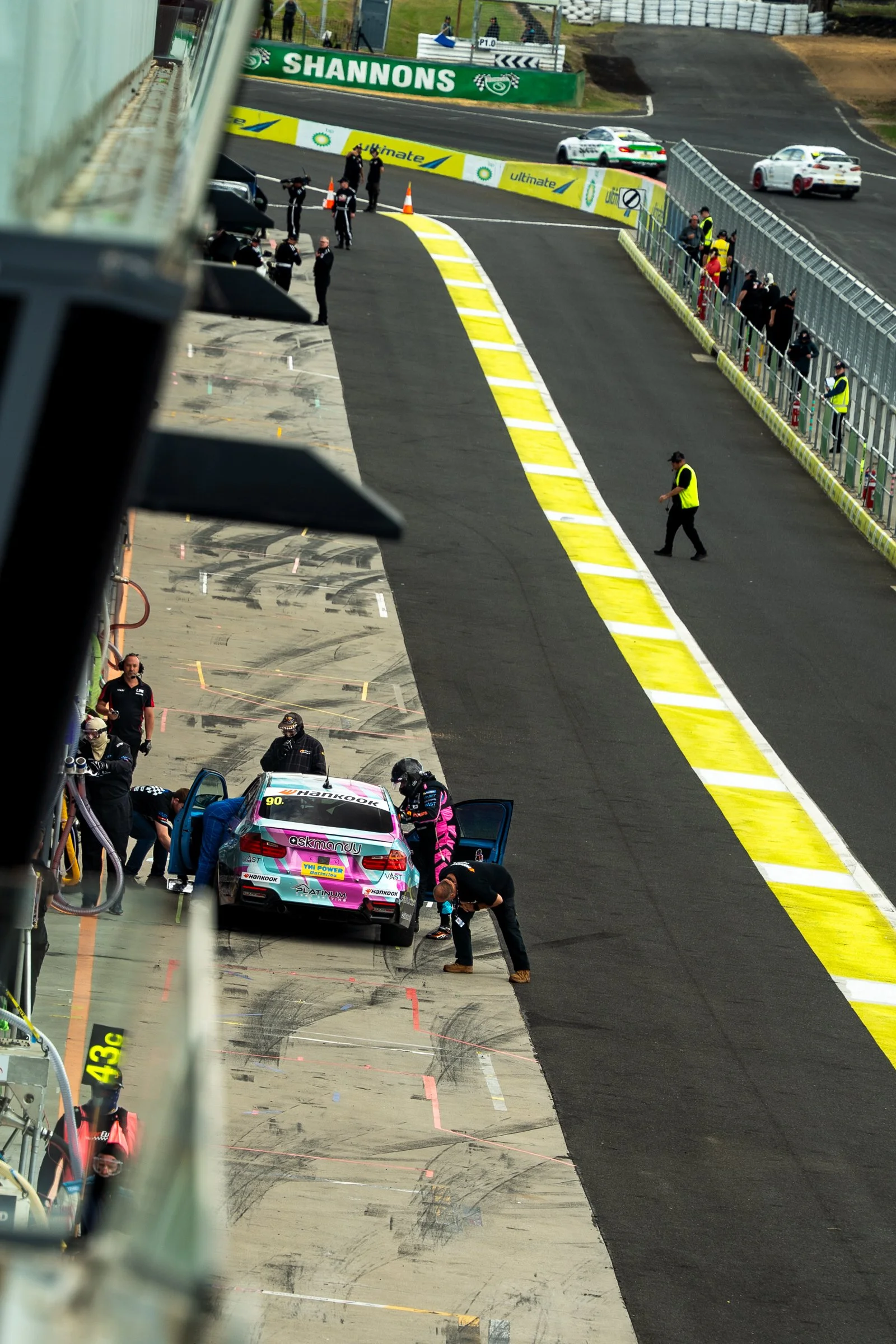 Overhead view of the Flip Side BMW in pit lane with doors open as driver Amar Sharma stands beside the car while crew work on it during the Bathurst 6 Hour