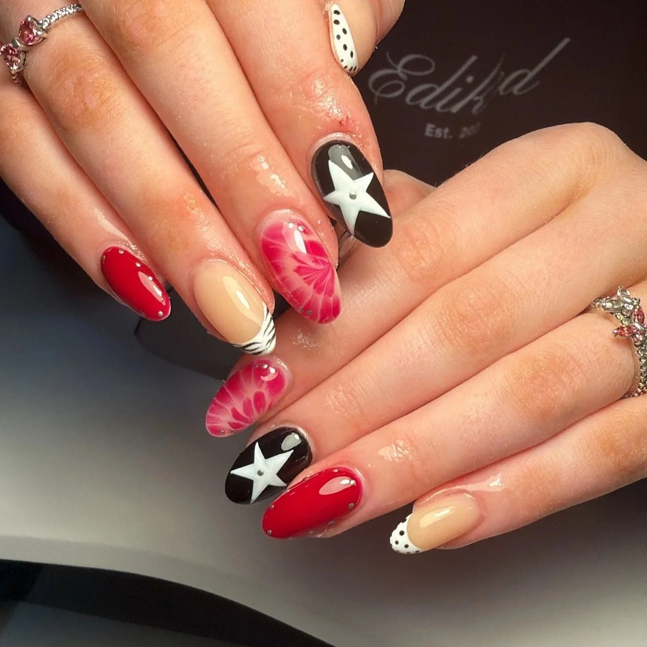 Close-up of a woman's hands with manicured nails featuring various designs, including stars, flowers, and polka dots in red, black, beige, and white colors.