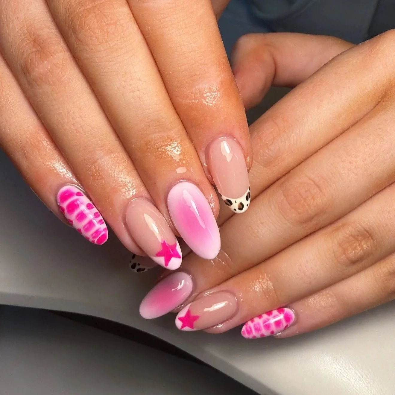 Close-up of hands with manicured nails featuring pink and white designs, including stars, zebra pattern, checkered pattern, and pink gradient