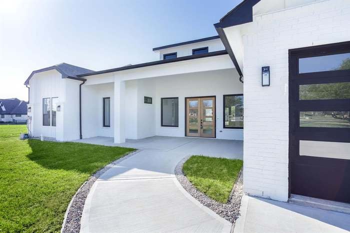 Modern white house with black trim and a curved concrete walkway leading to the front door, green lawn on both sides, and clear blue sky