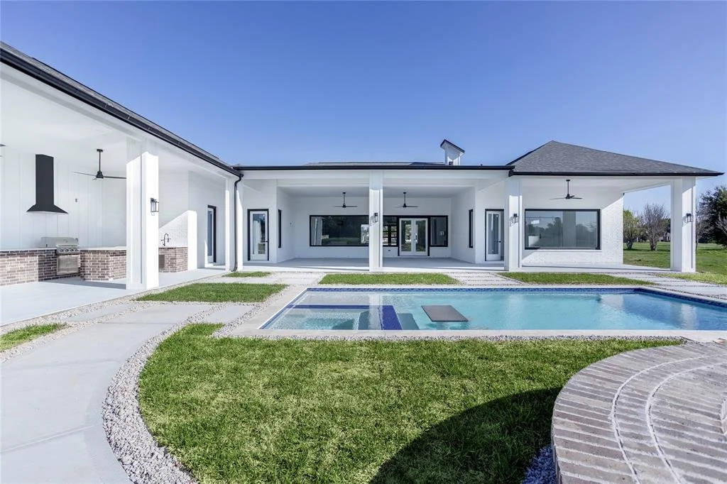 Modern white house with large covered patio, swimming pool, and landscaped yard under clear blue sky.