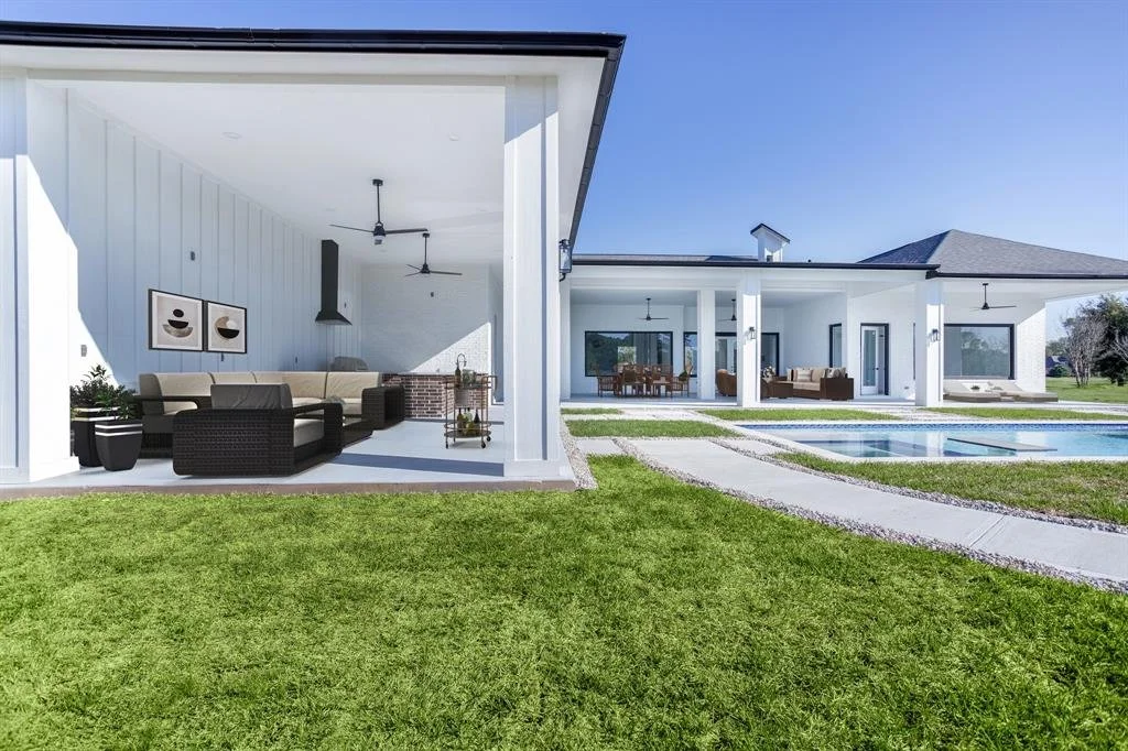 Modern house with outdoor living area, pool, and green lawn under a clear blue sky.