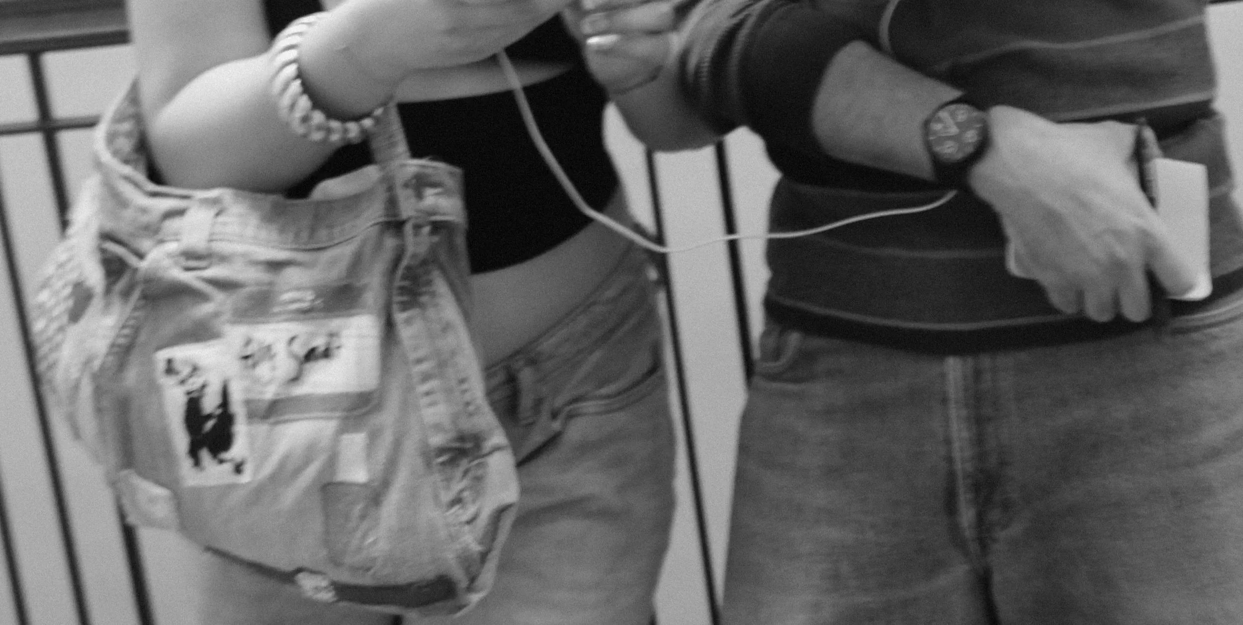 Two people standing next to each other, one with a backpack and the other holding a vintage MP3 player. The person on the left is wearing a bracelet and a denim patchwork purse the person on the right is wearing a patchwork shirt and vintage watch.