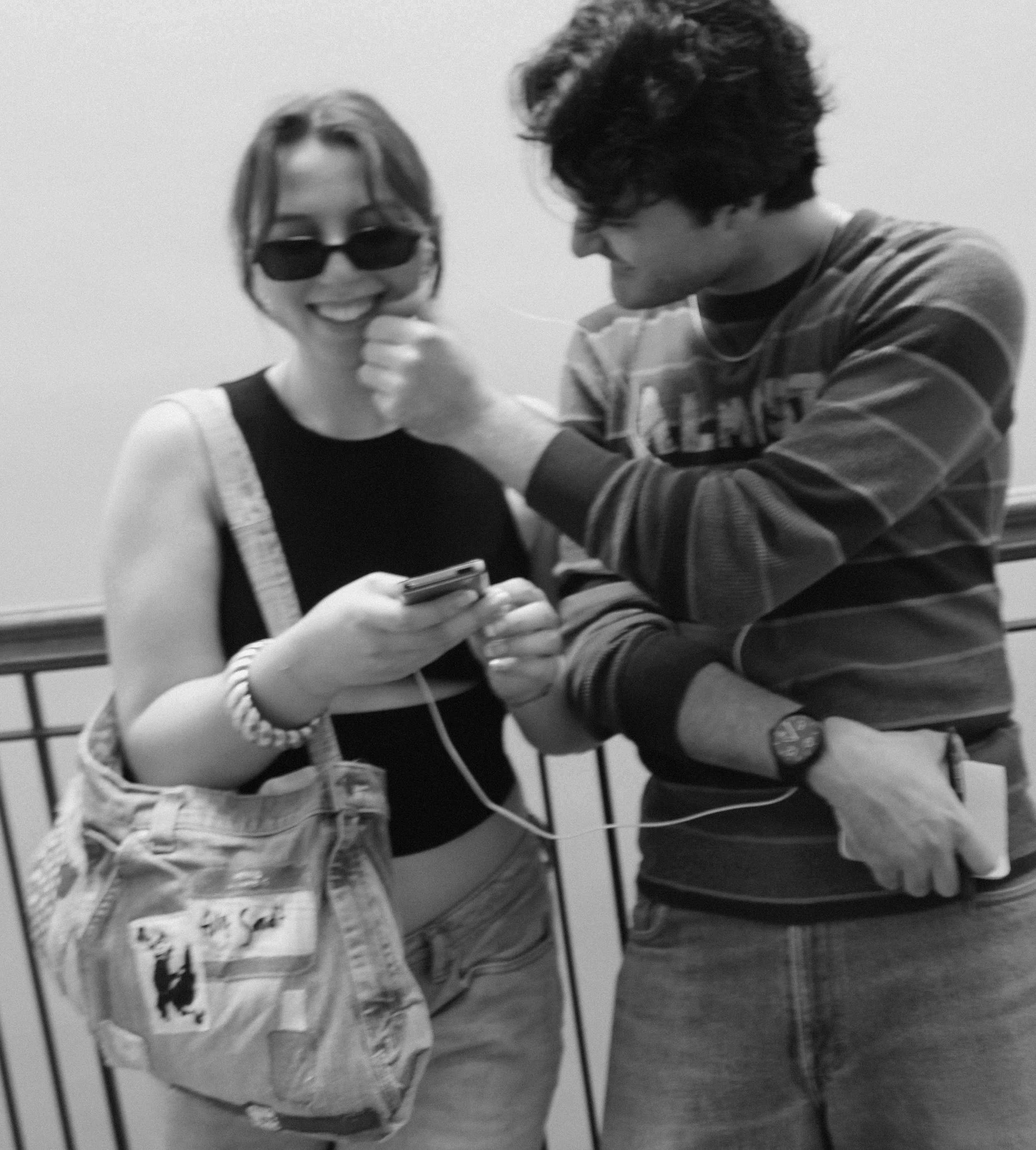 A woman smiling, wearing sunglasses, with a woman and a man, appears to be sharing a moment of amusement or fun, with the woman holding an mp3 player and the man touching her chin.