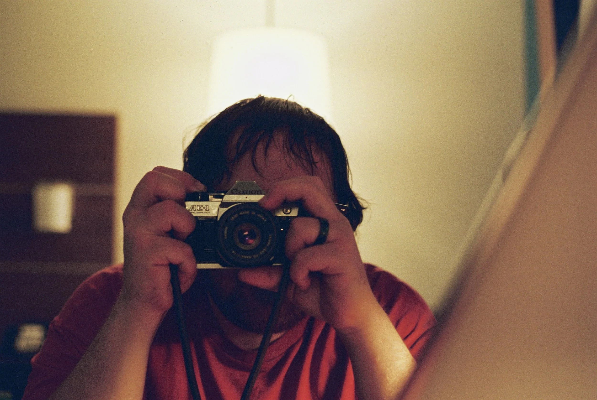 Person taking a mirror selfie with a vintage camera in a dimly lit room.