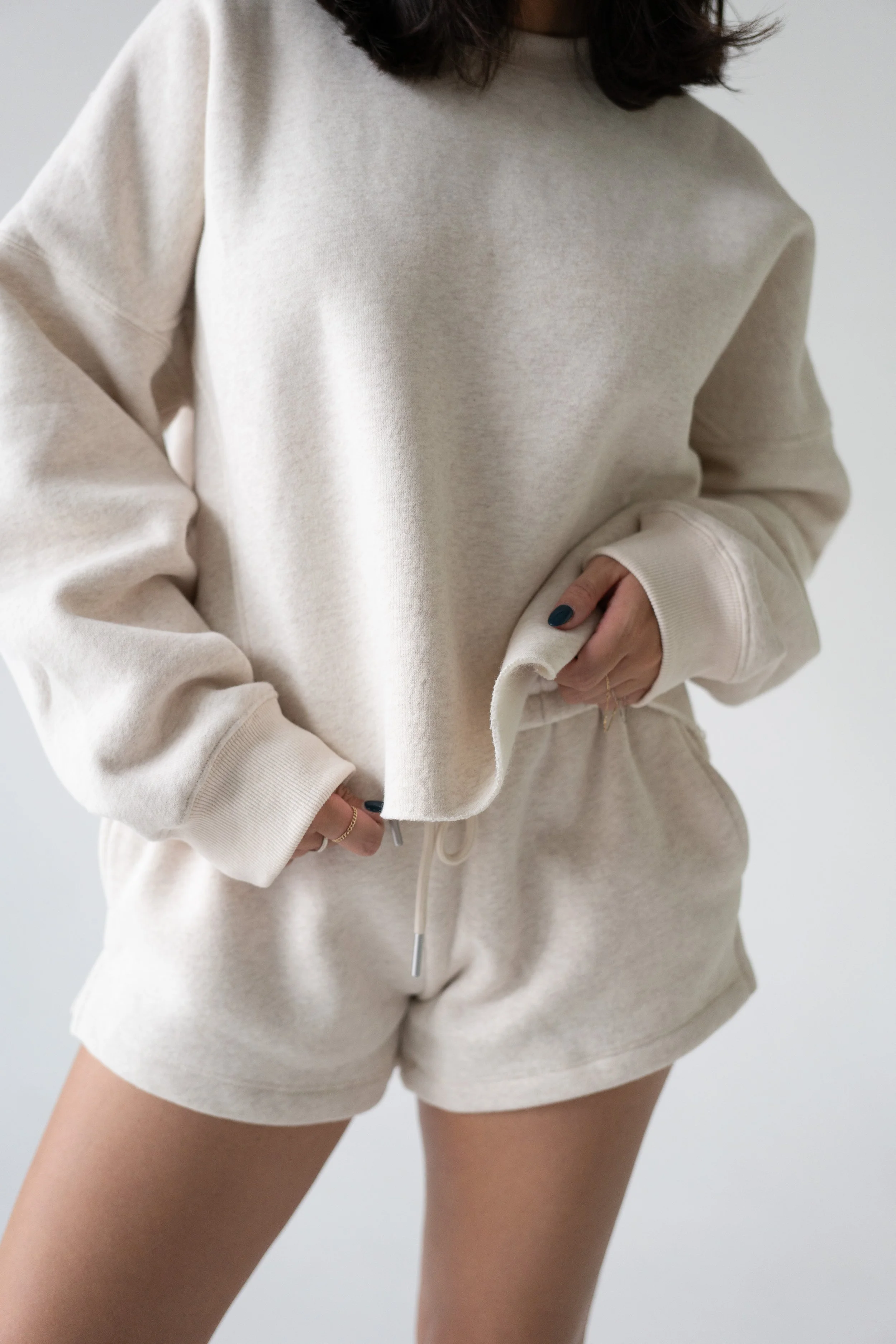 Person wearing a beige sweatshirt and matching sweat shorts, with their hand in the pocket of the shorts.