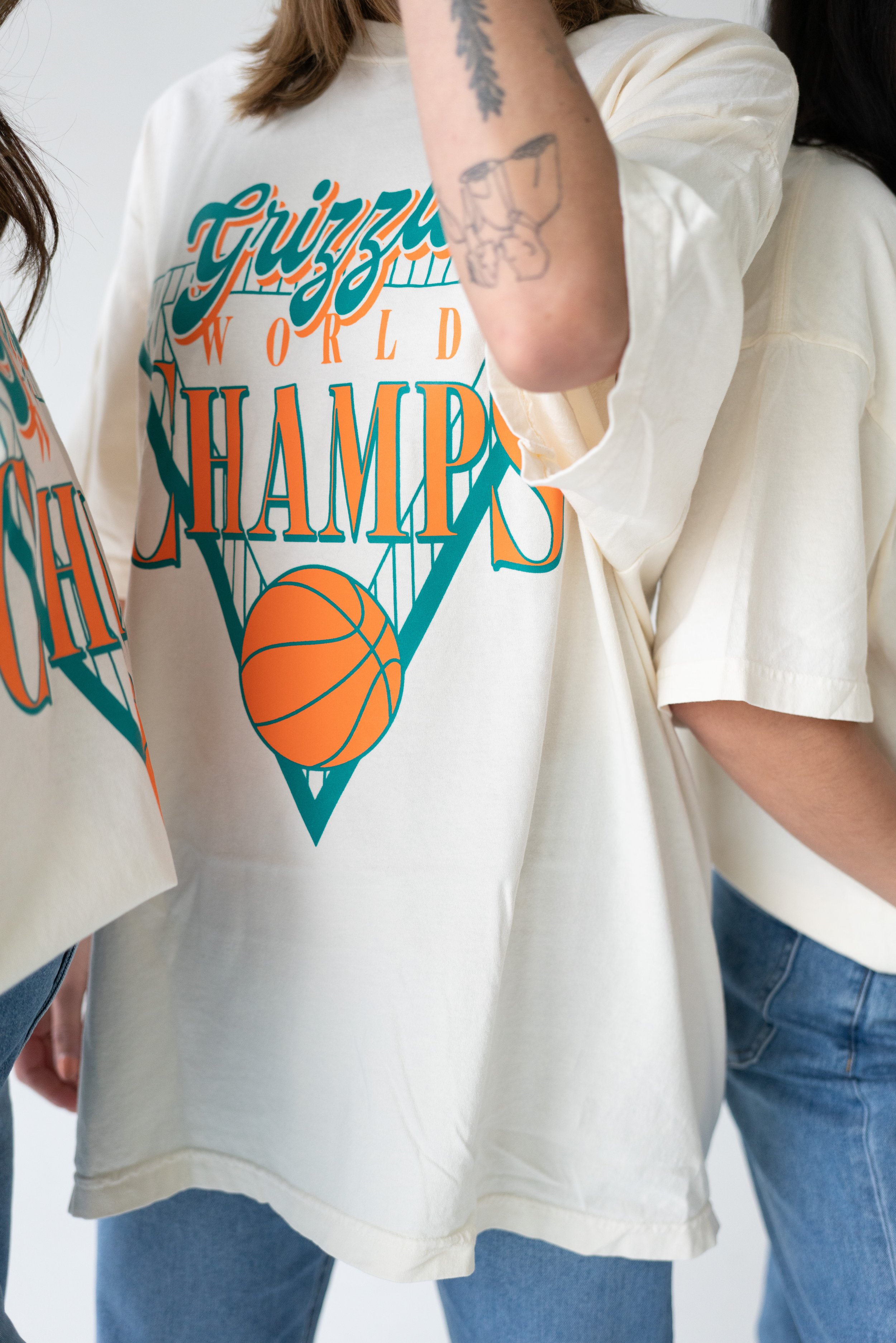 Person wearing a white T-shirt with a graphic design celebrating the championship of the New York Knicks basketball team, showing a basketball going through a hoop.