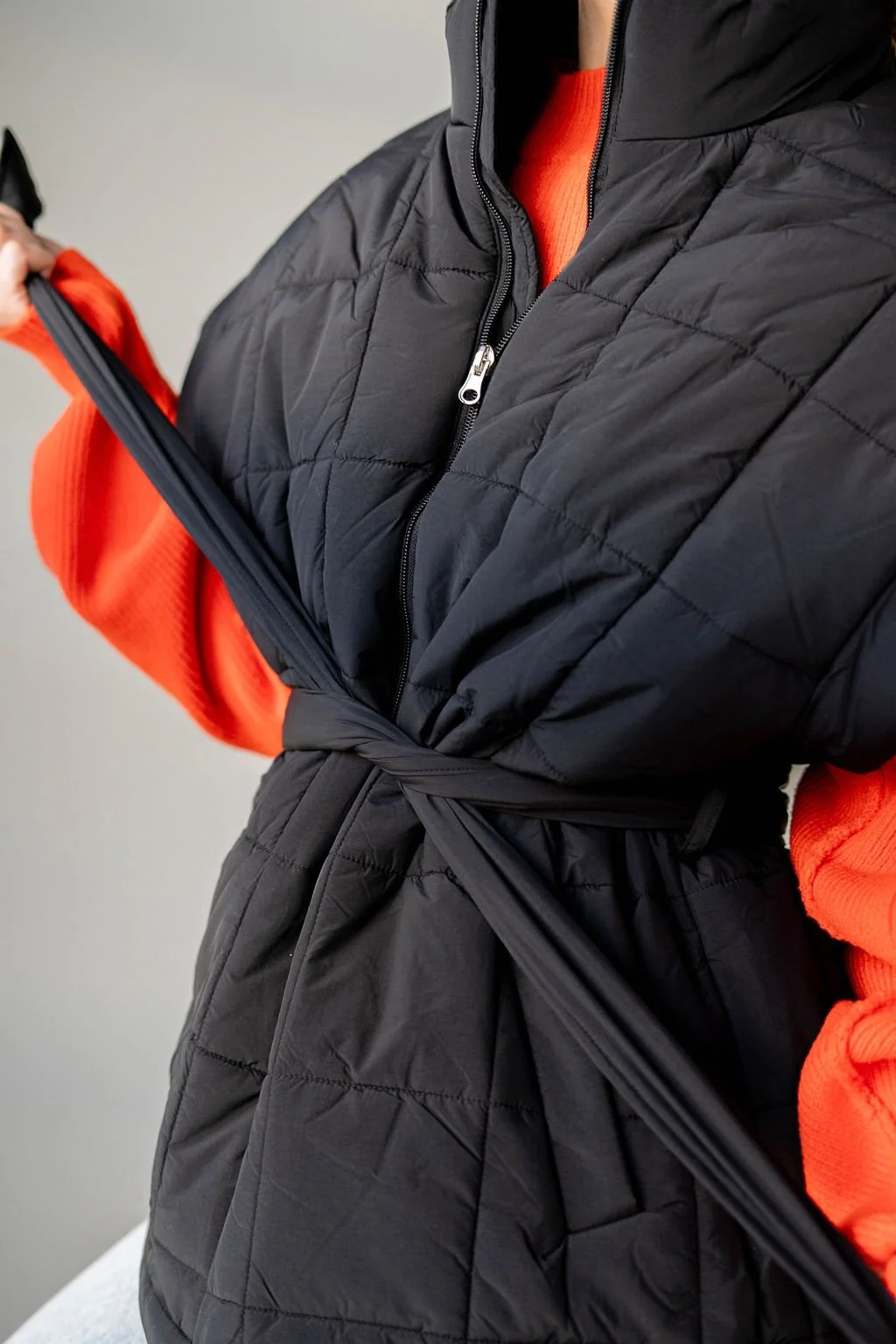 Person wearing a black puffer jacket and orange sweater, holding the jacket open.