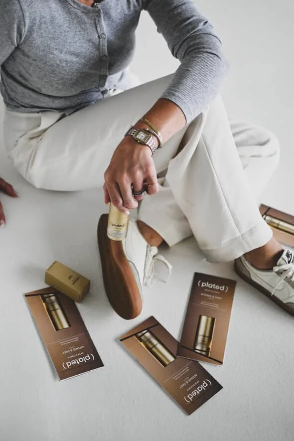 A person sitting on the floor with their legs crossed, holding a bottle of skincare product. There are several skincare product boxes and a small gold box scattered on the floor around them.
