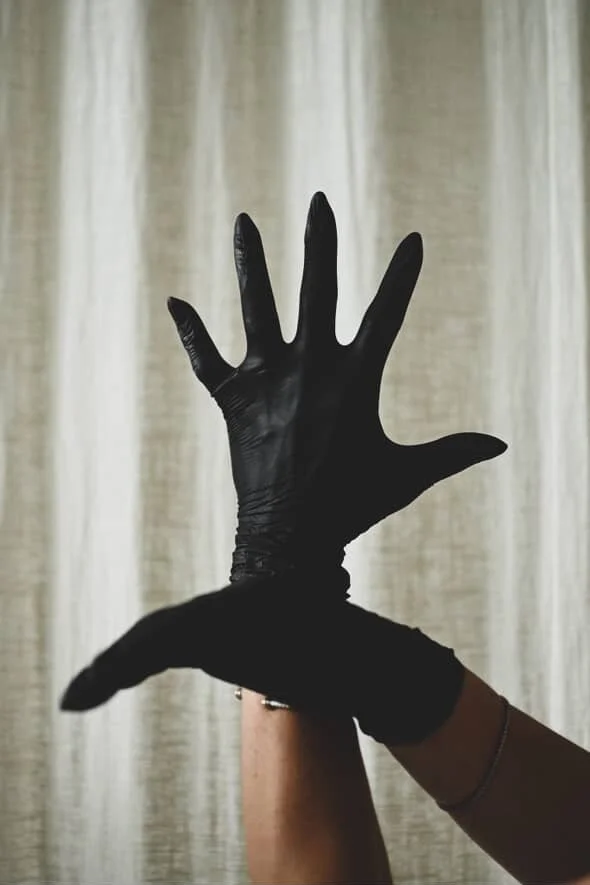 Two hands, one with a black glove, in an artistic pose against a neutral curtain background.