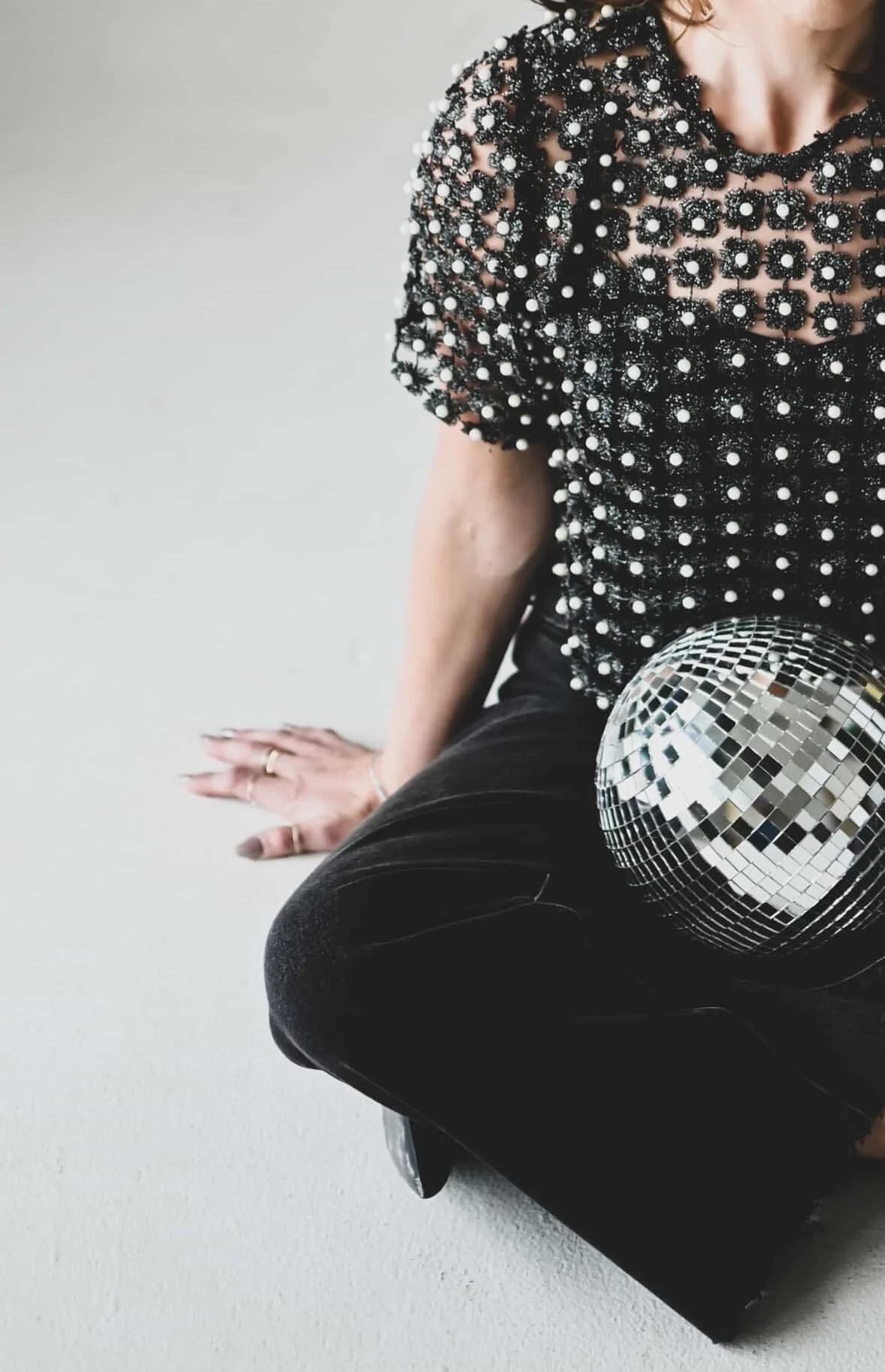 Person wearing a black top with white embellishments, black pants, sitting on the floor with a disco ball nearby.