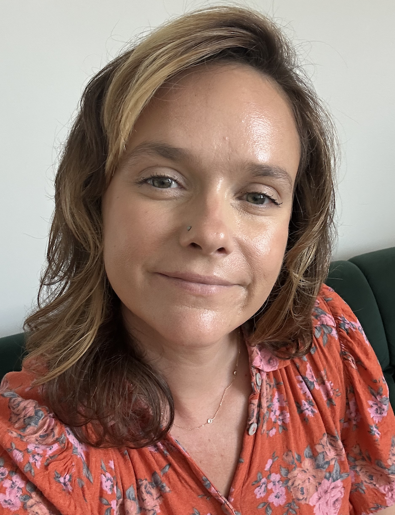 A woman with shoulder-length light brown hair, wearing a red floral blouse, smiling softly at the camera.