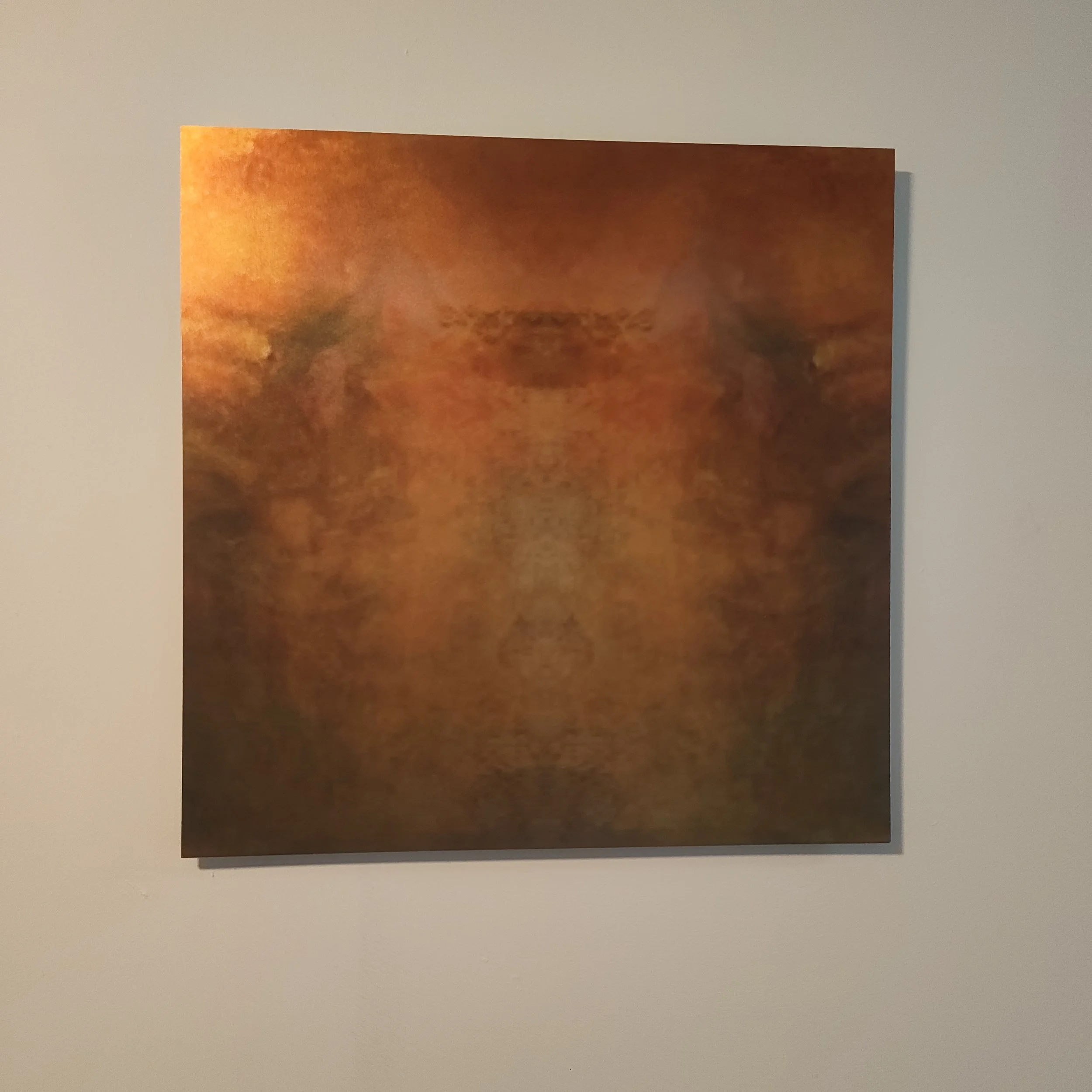 Abstract printed artwork with warm orange, yellow, and brown hues, mounted on a white wall.