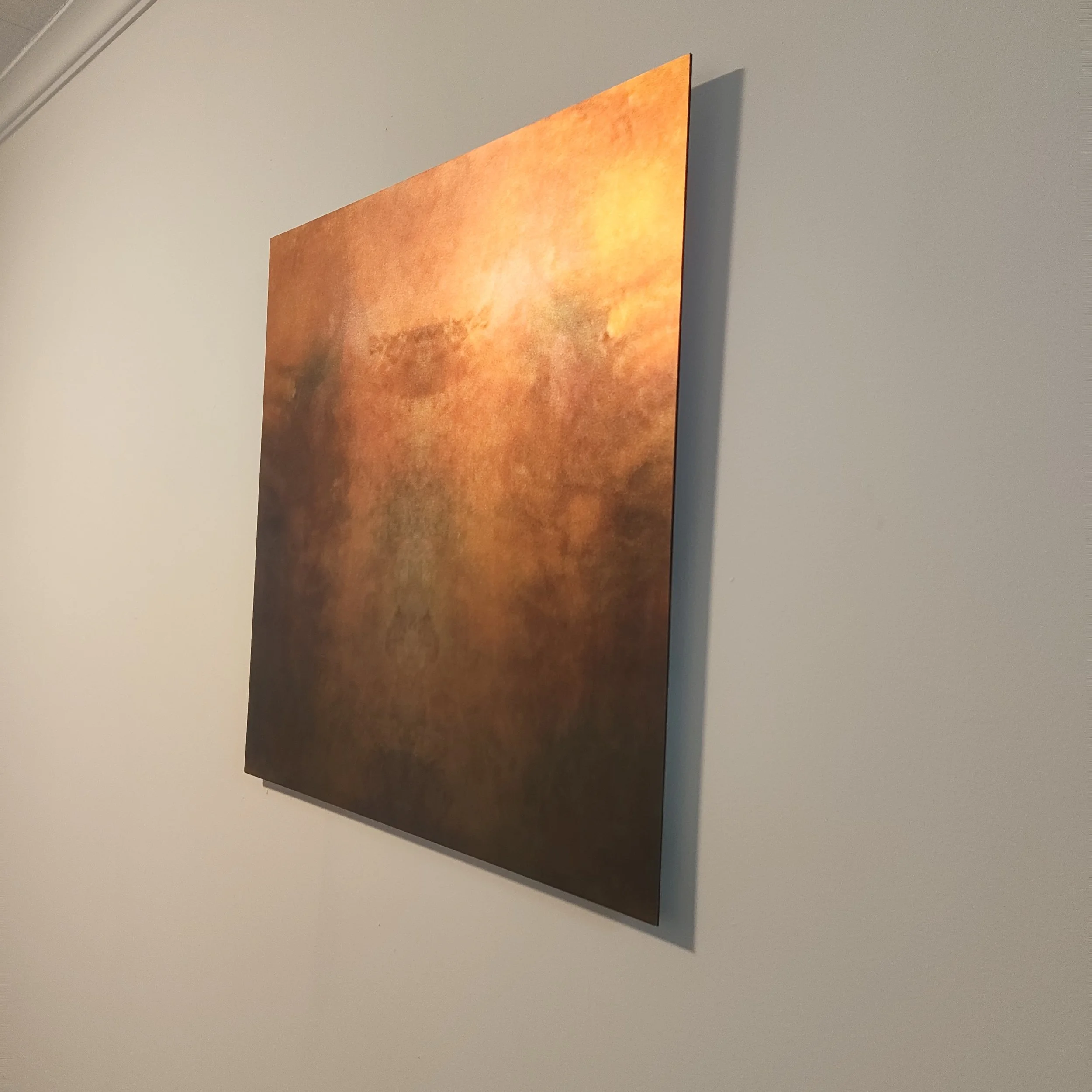 A partially visible abstract painting with warm orange and yellow tones hangs on a plain light-colored wall.
