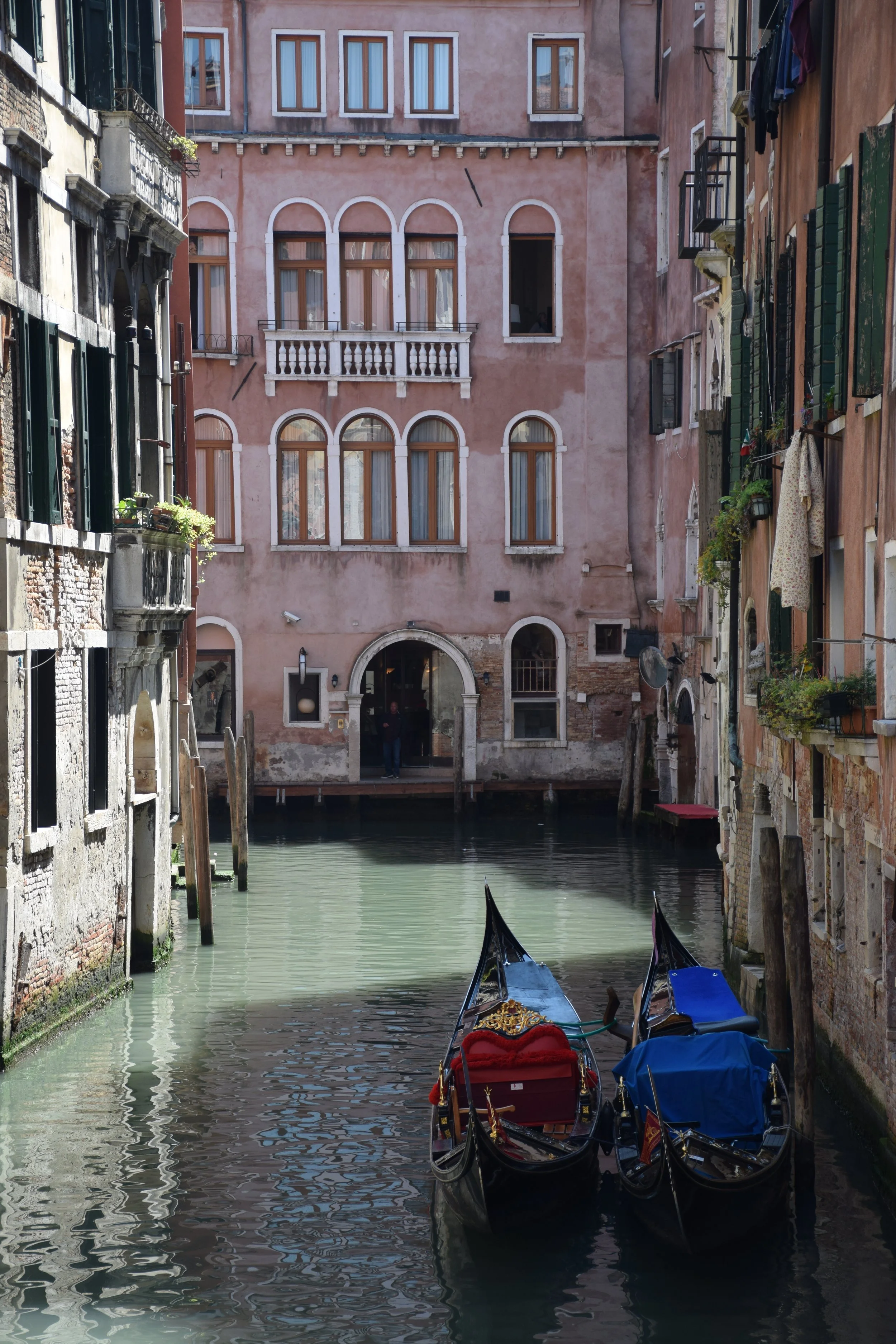 Gondolas docked along a canal in Venice, Italy, with colorful historic buildings in the background and laundry hanging outside on the right.