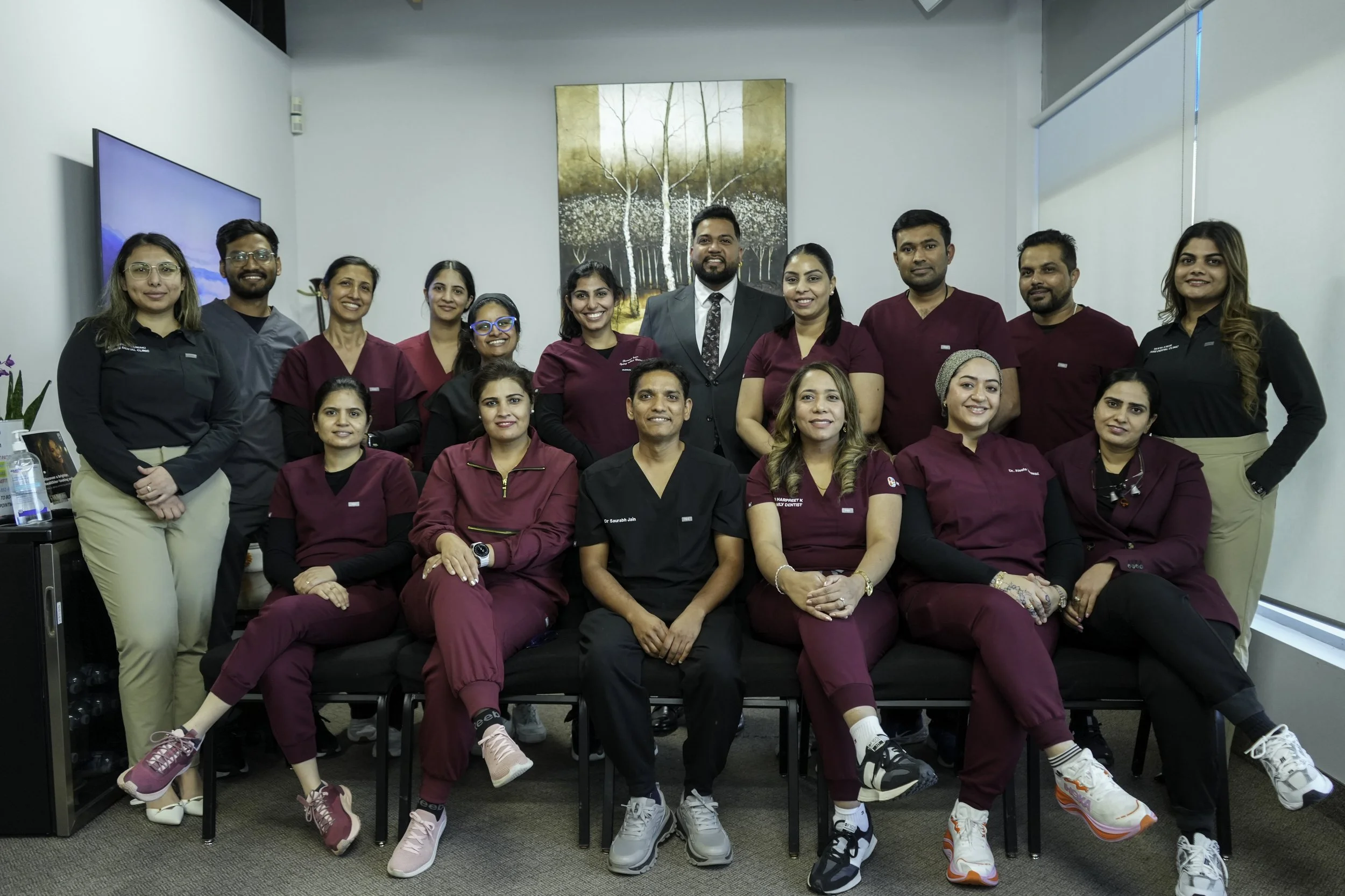 Group of healthcare professionals, including doctors and nurses, posing for a photo in a medical office or clinic, with a large window and artwork in the background.