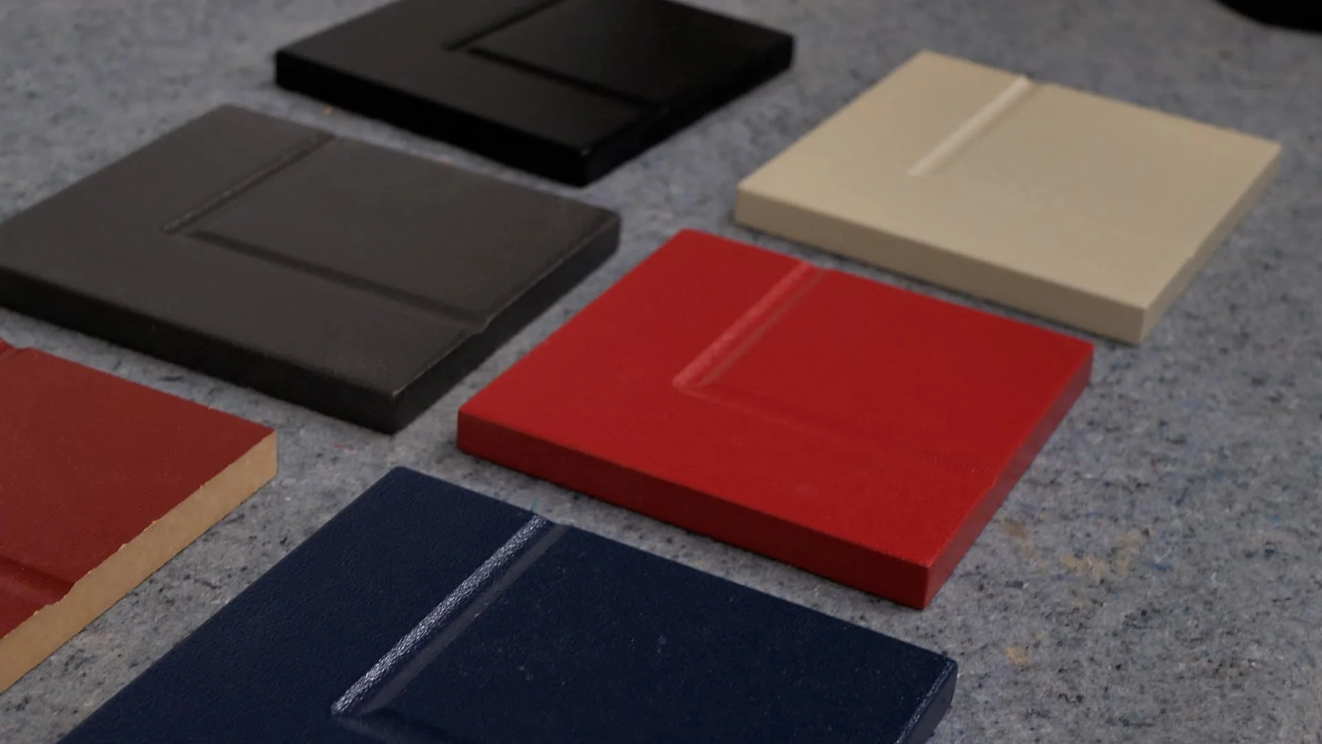 Several square tiles in black, red, beige, gray, and navy blue are arranged on a gray surface.