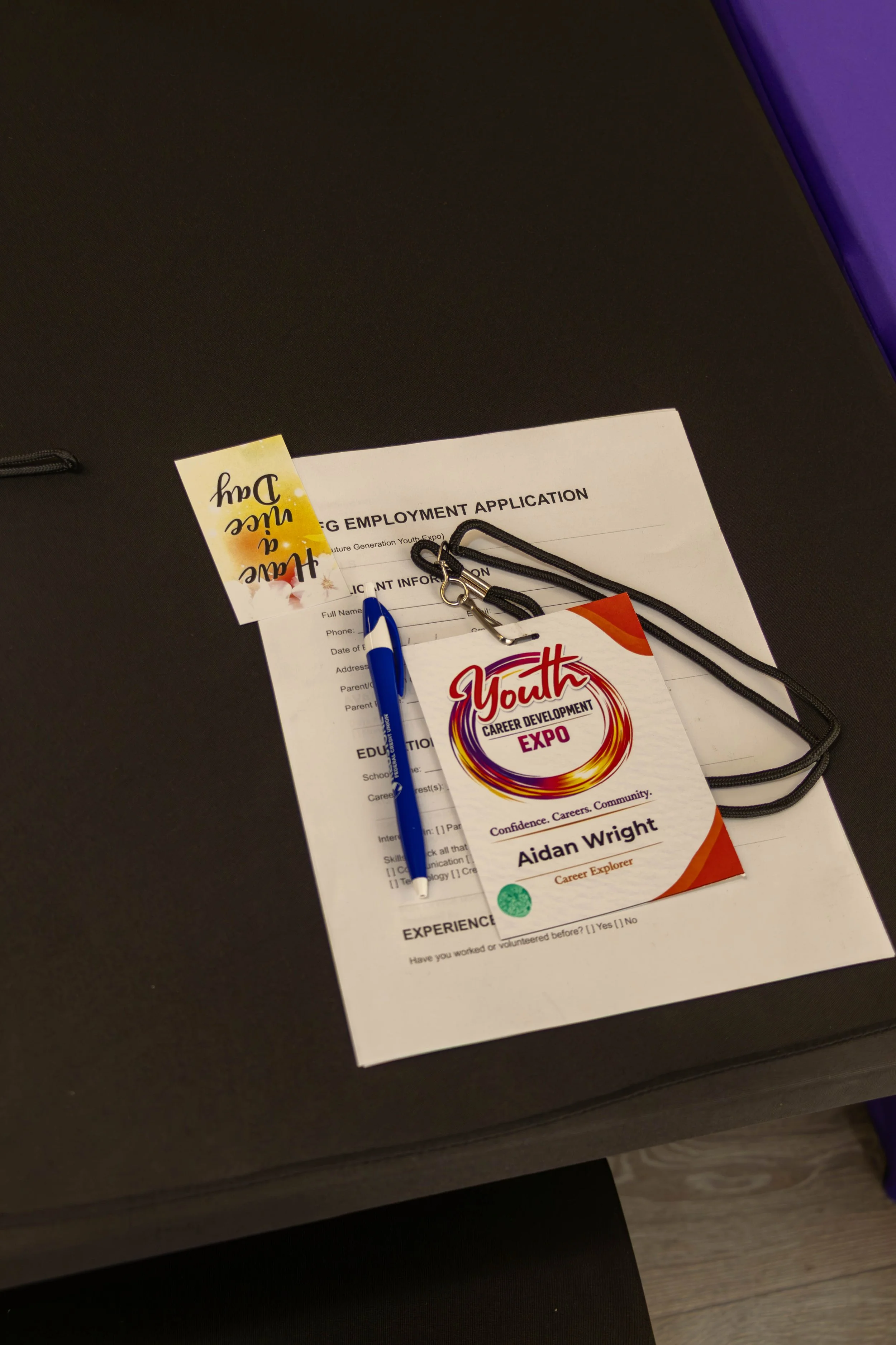 Career development expo name tag, application form, blue and white pen, and lanyard with a badge on a dark table.
