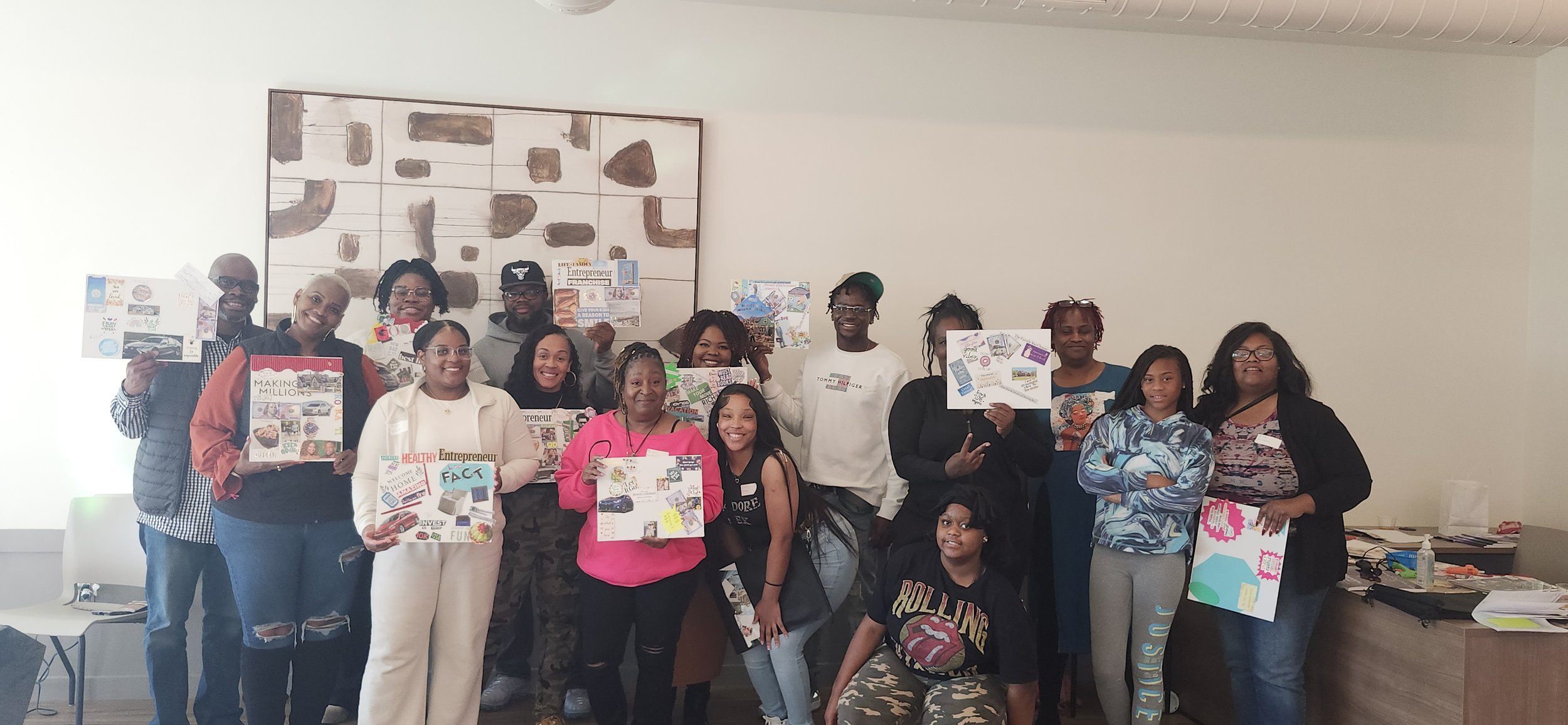 Group of diverse people holding colorful posters and flyers in a room with a white wall and abstract artwork.