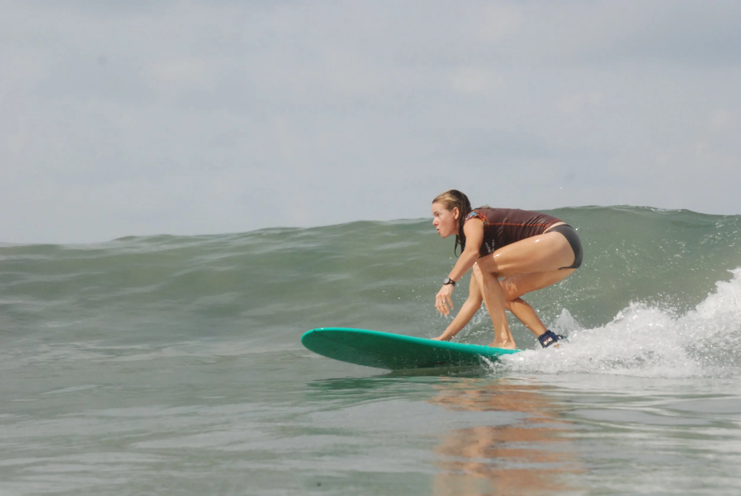 A person with long hair surfing on a green surfboard in the ocean, crouching low on the wave.
