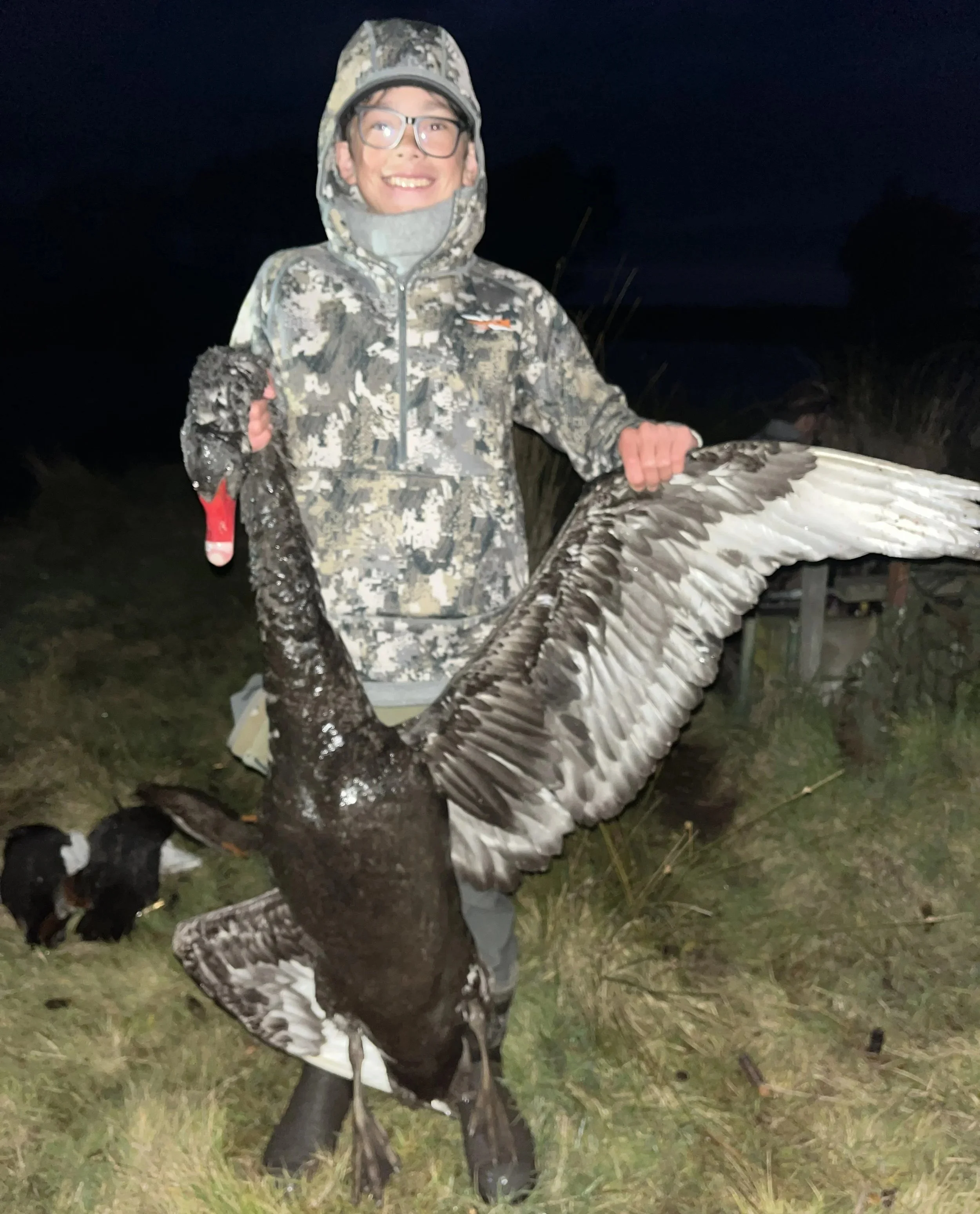 A young person in camouflage clothing holding a large bird with its wings spread open, standing outdoors at night.