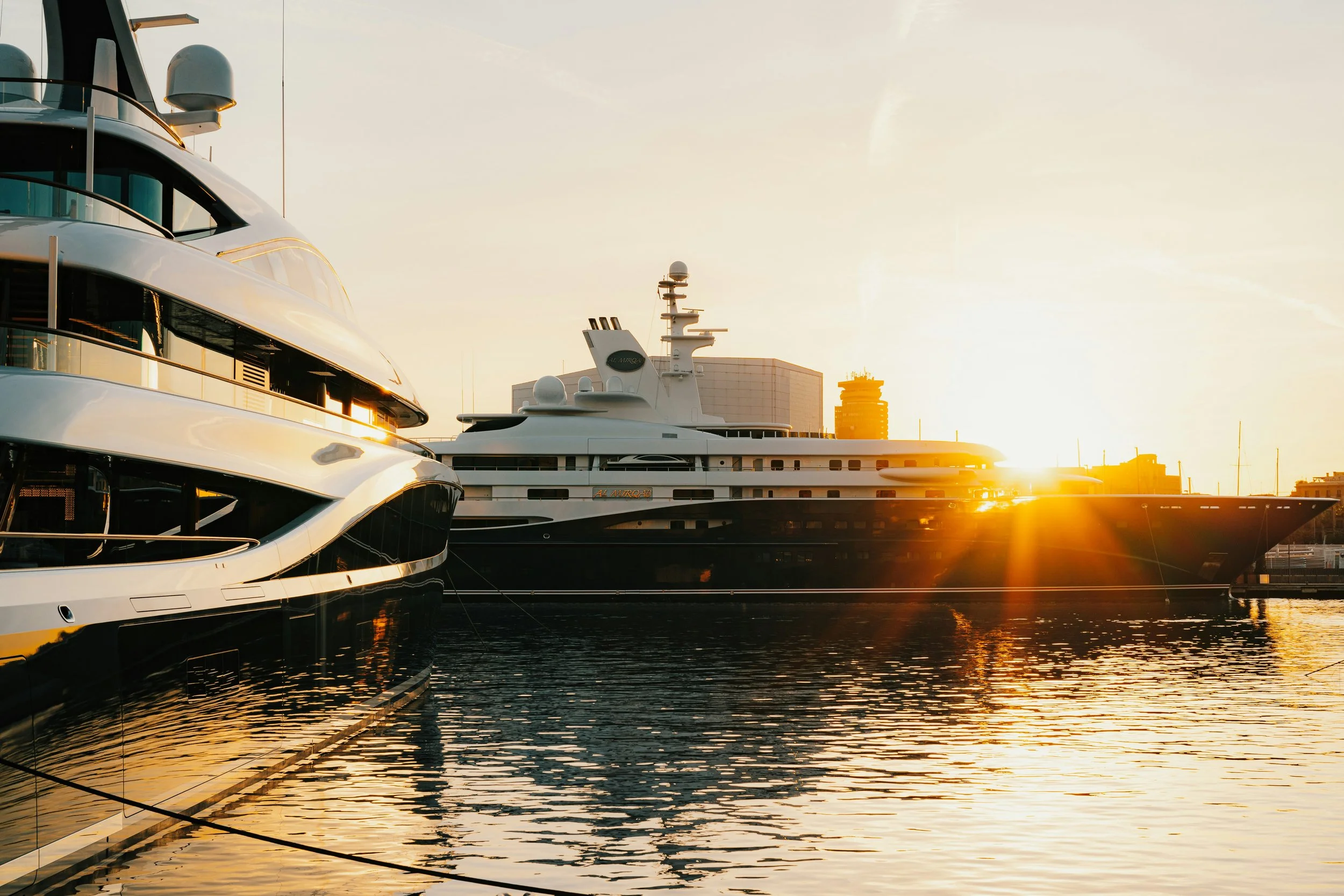 Multiple yachts docked at a marina with the setting sun in the background, creating a warm glow on the water.