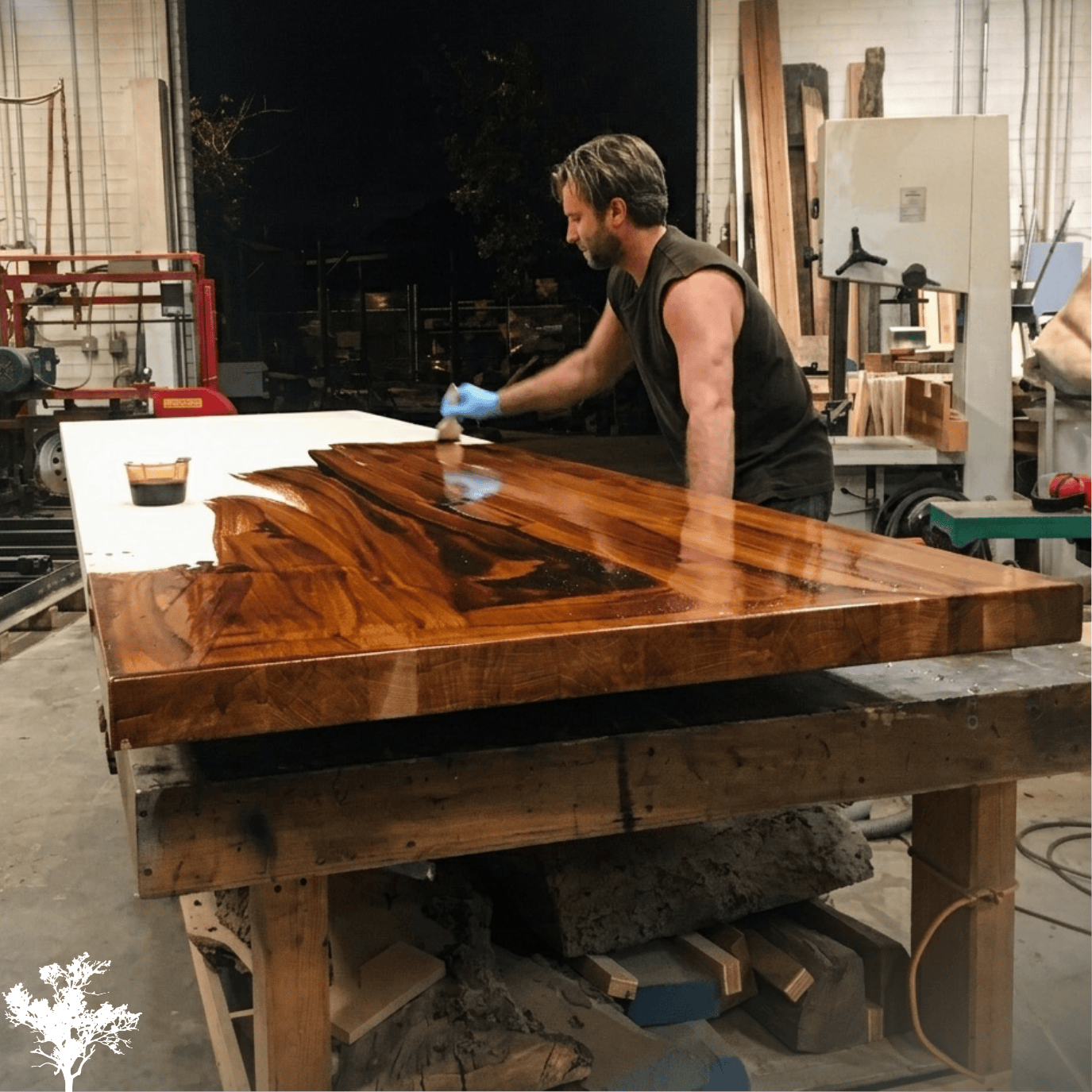 A man working on a large, polished wooden table in a workshop at night.