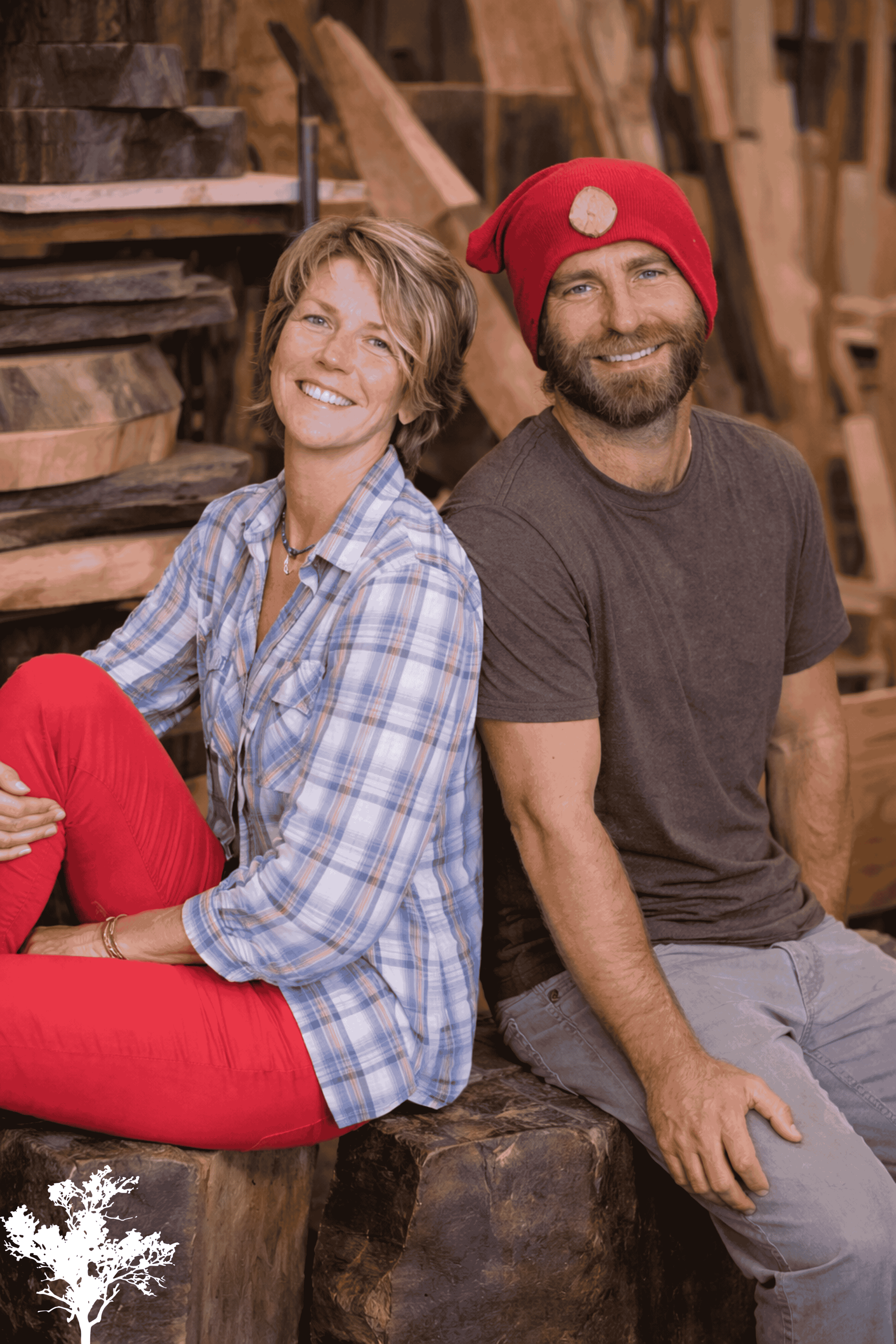 A smiling woman and man sitting on a wooden bench in a woodworking shop, with wood pieces and tools in the background.