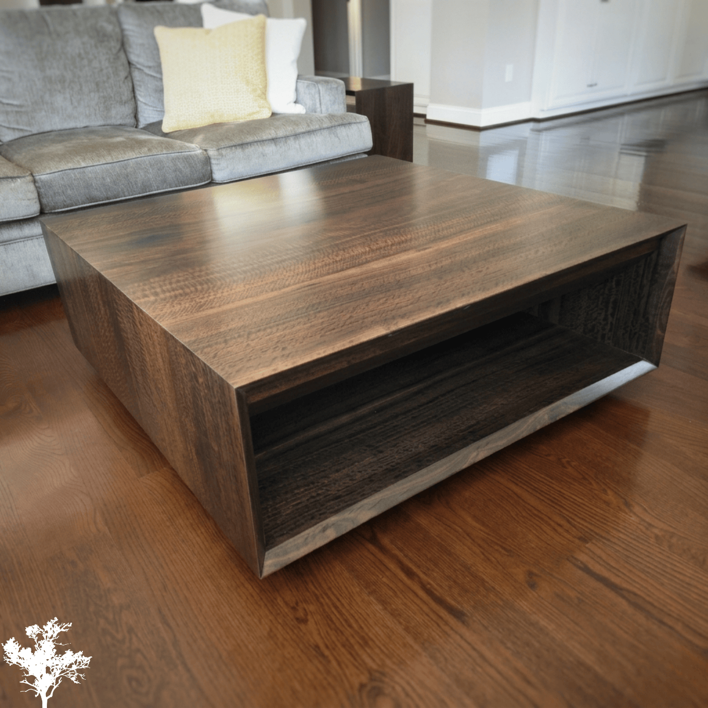 A wooden coffee table with an open shelf in a living room with hardwood floors and a gray sofa.