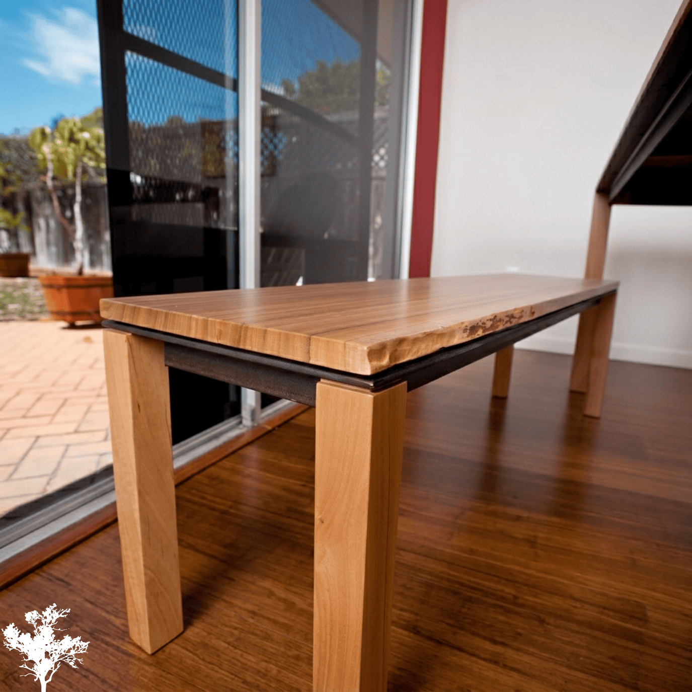 Close-up of a wooden bench with a natural finish, located indoors near a sliding glass door leading outside.
