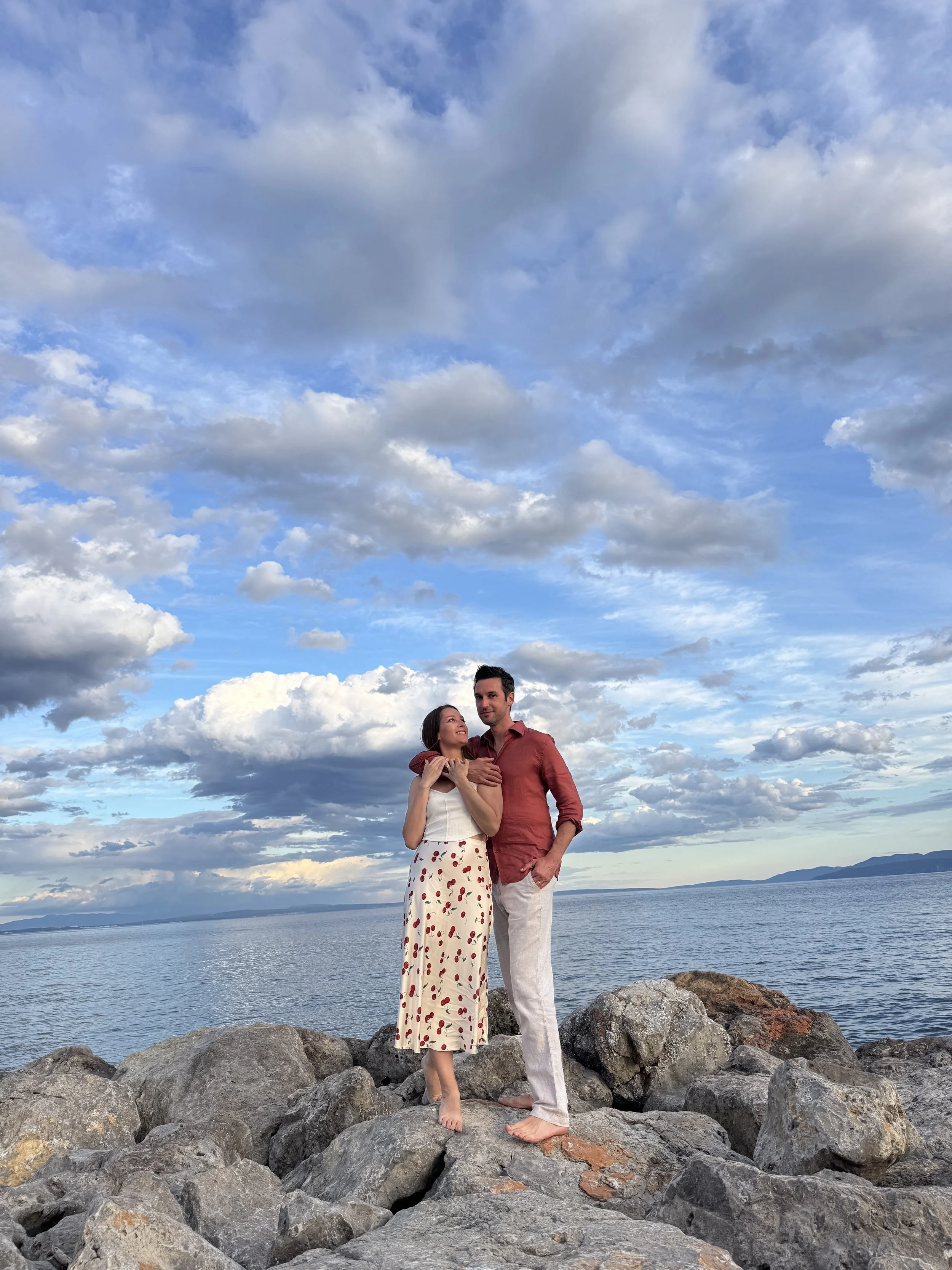 Couple standing on rocks with the ocean and blue sky behind them