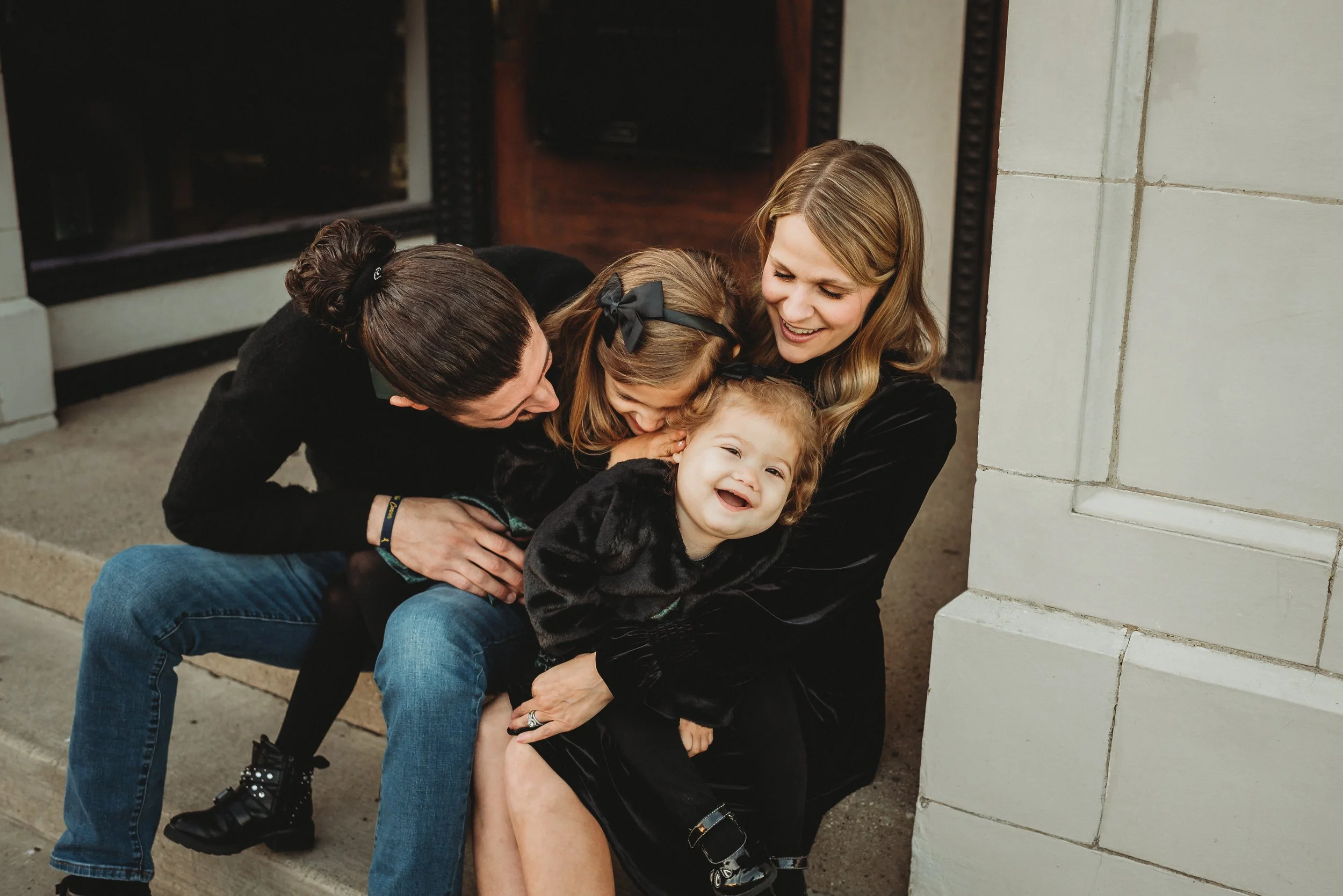 Four women and a young girl sharing a joyful moment outside a building, sitting on a step.