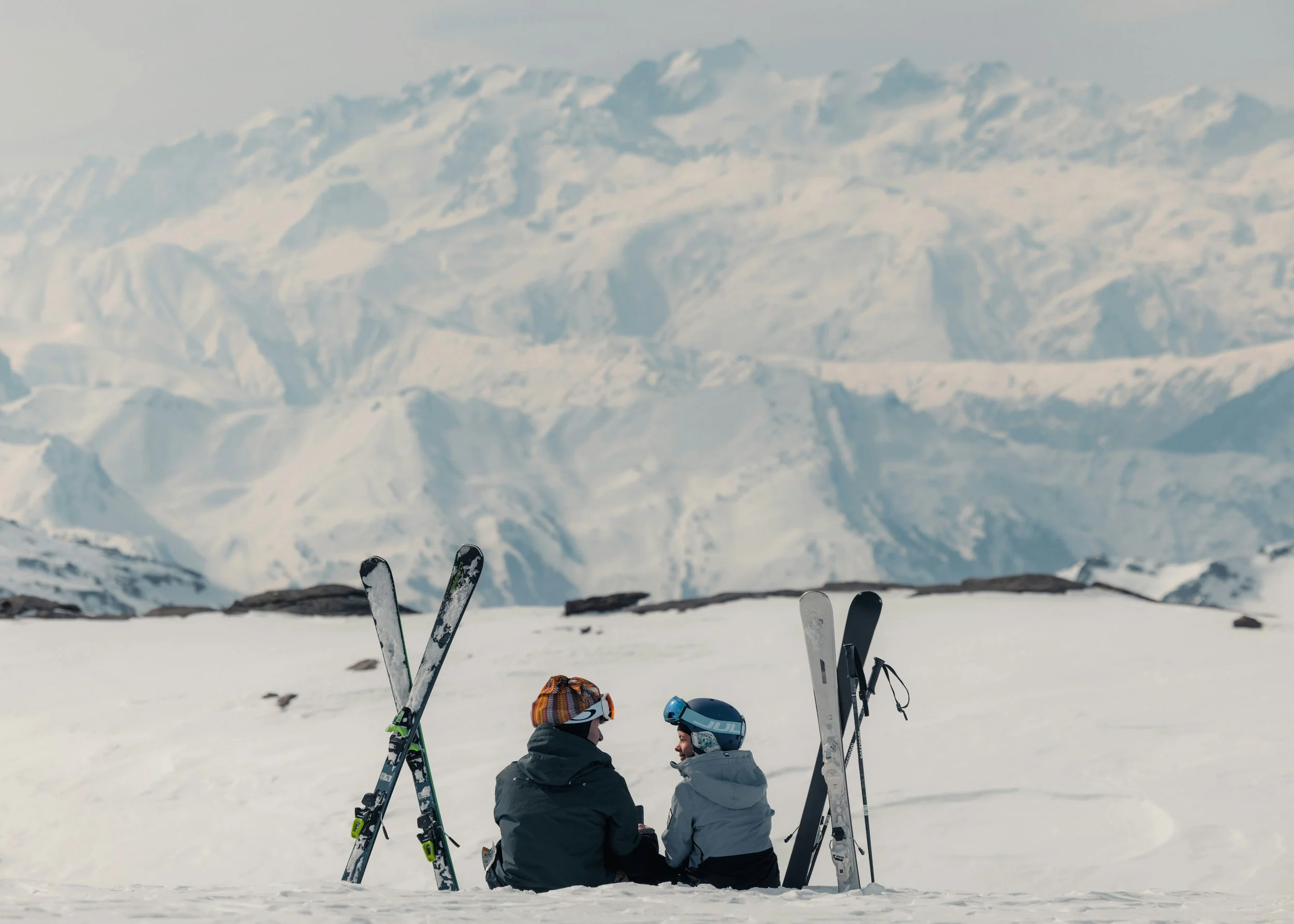 Two people with skiis in the snow talking on a mountain