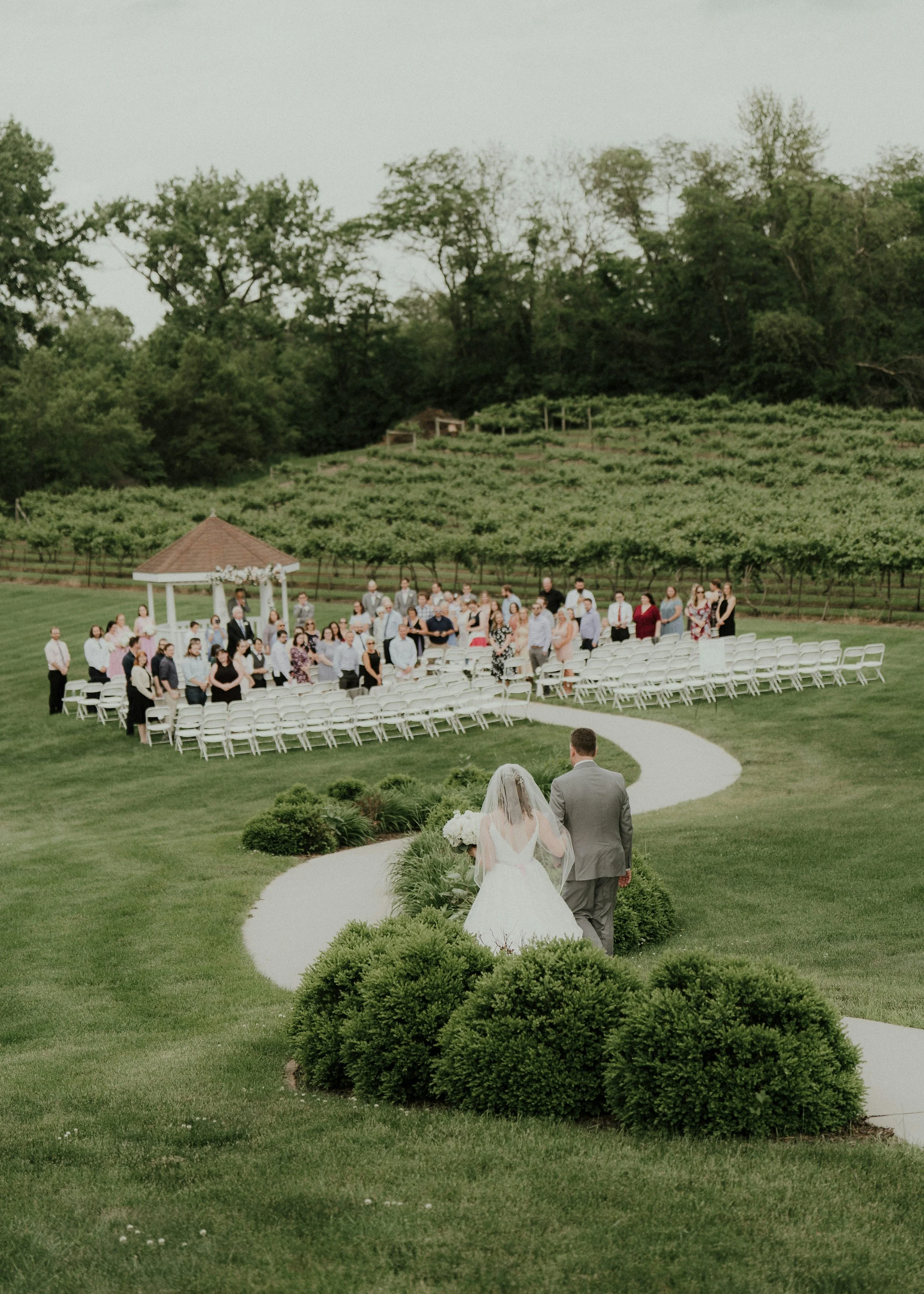 Wedding in a big green paddock. Ceremony with everyone standing up, watching a male and female couple walk down the aisle