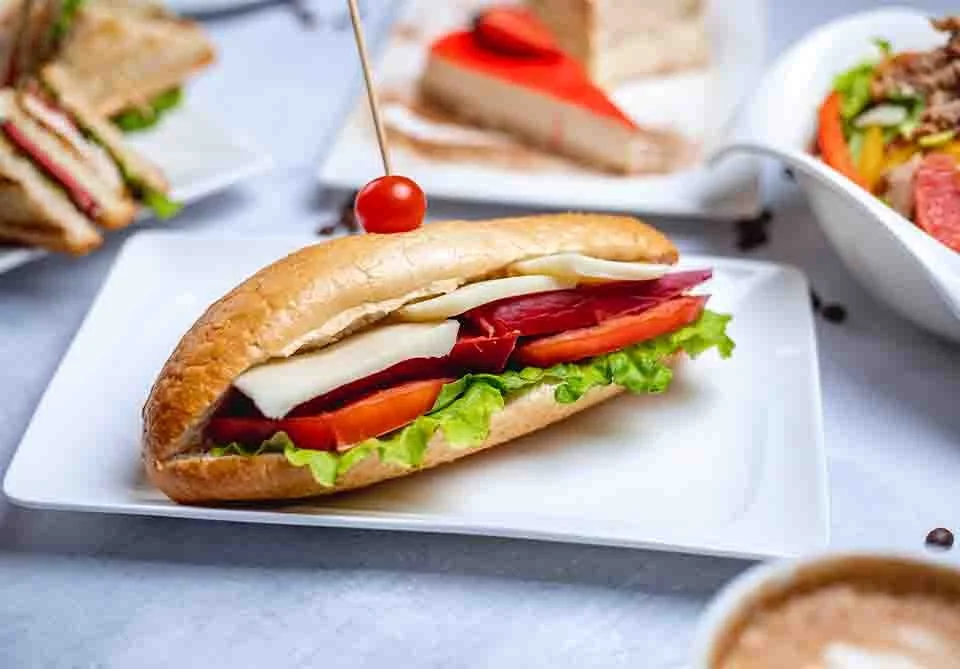 Turkey sandwich with lettuce, tomato, cheese, red pepper and cherry on a bun