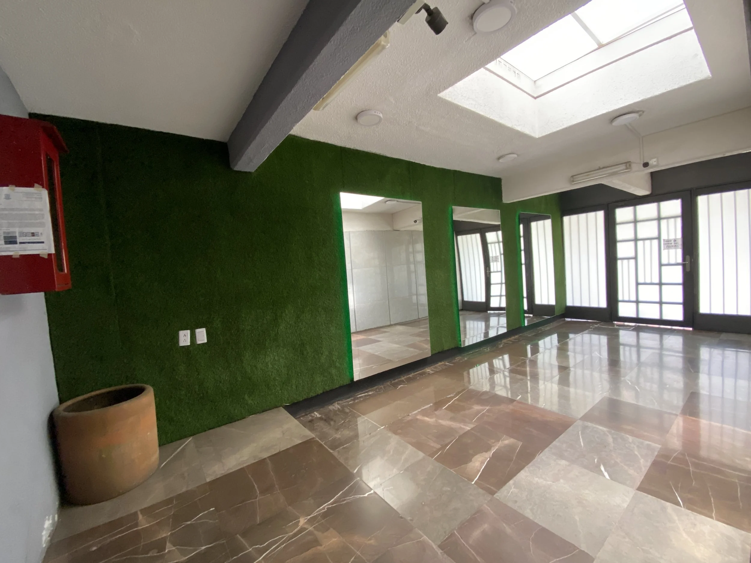 Lobby area with green wall, large beige flower pot, marble tile flooring, glass doors, and skylight overhead.