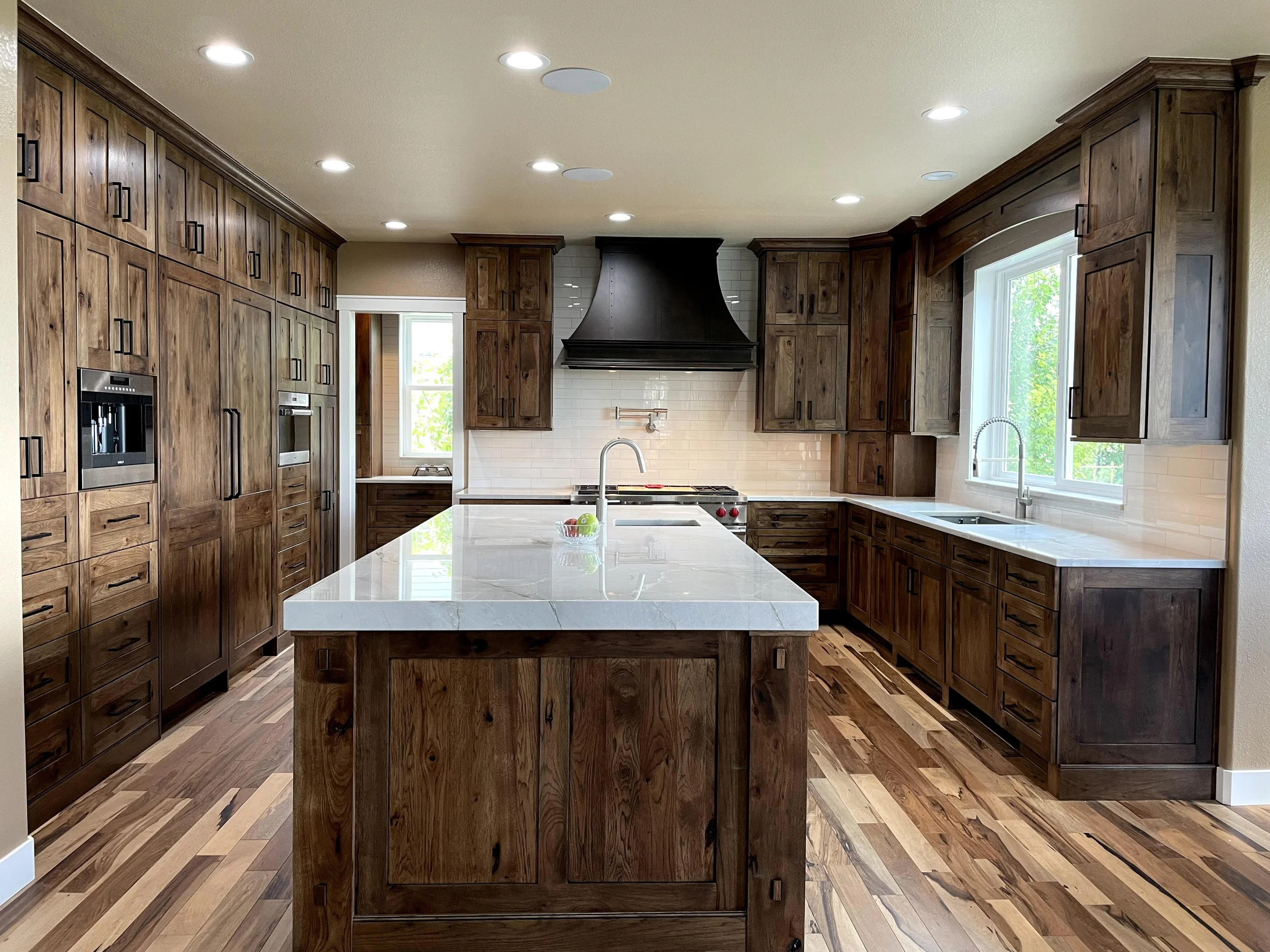 Timeless kitchen with hickory wood cabinets, quartz countertops, a large island, custom hood, built-in appliances and hardwood floors.