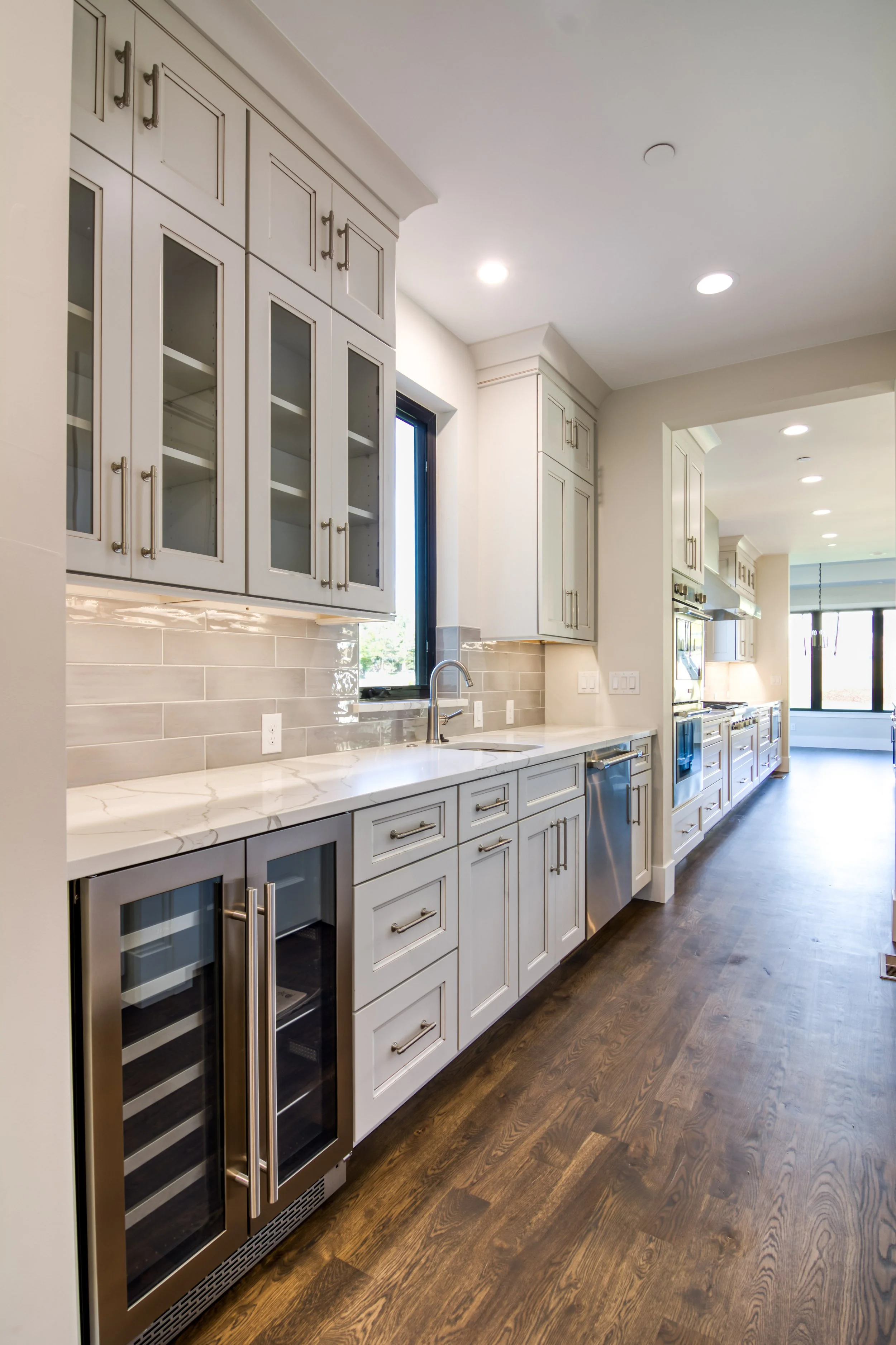 Modern kitchen with white painted cabinets, stainless steel appliances, a quartz countertop, and hardwood flooring.