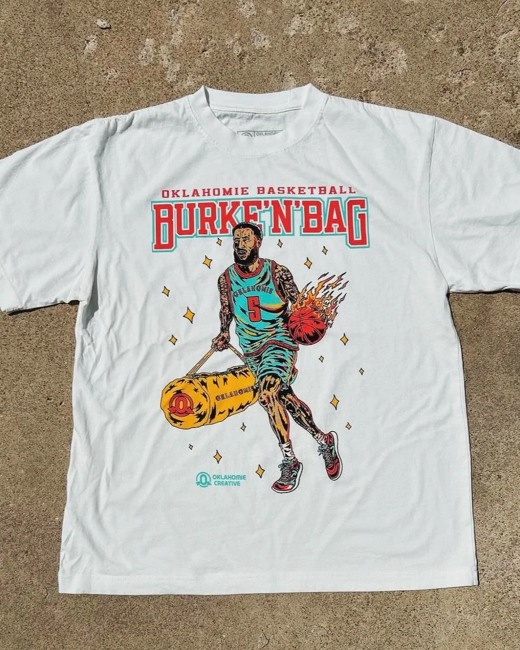 White t-shirt with a colorful graphic of a basketball player dribbling a flaming basketball, with text "Oklahomie Basketball" and "Burken' Bag" in bold letters. Drawn by Oklahomie Creative for Next22 YouTube basketball player Burke Putnam.