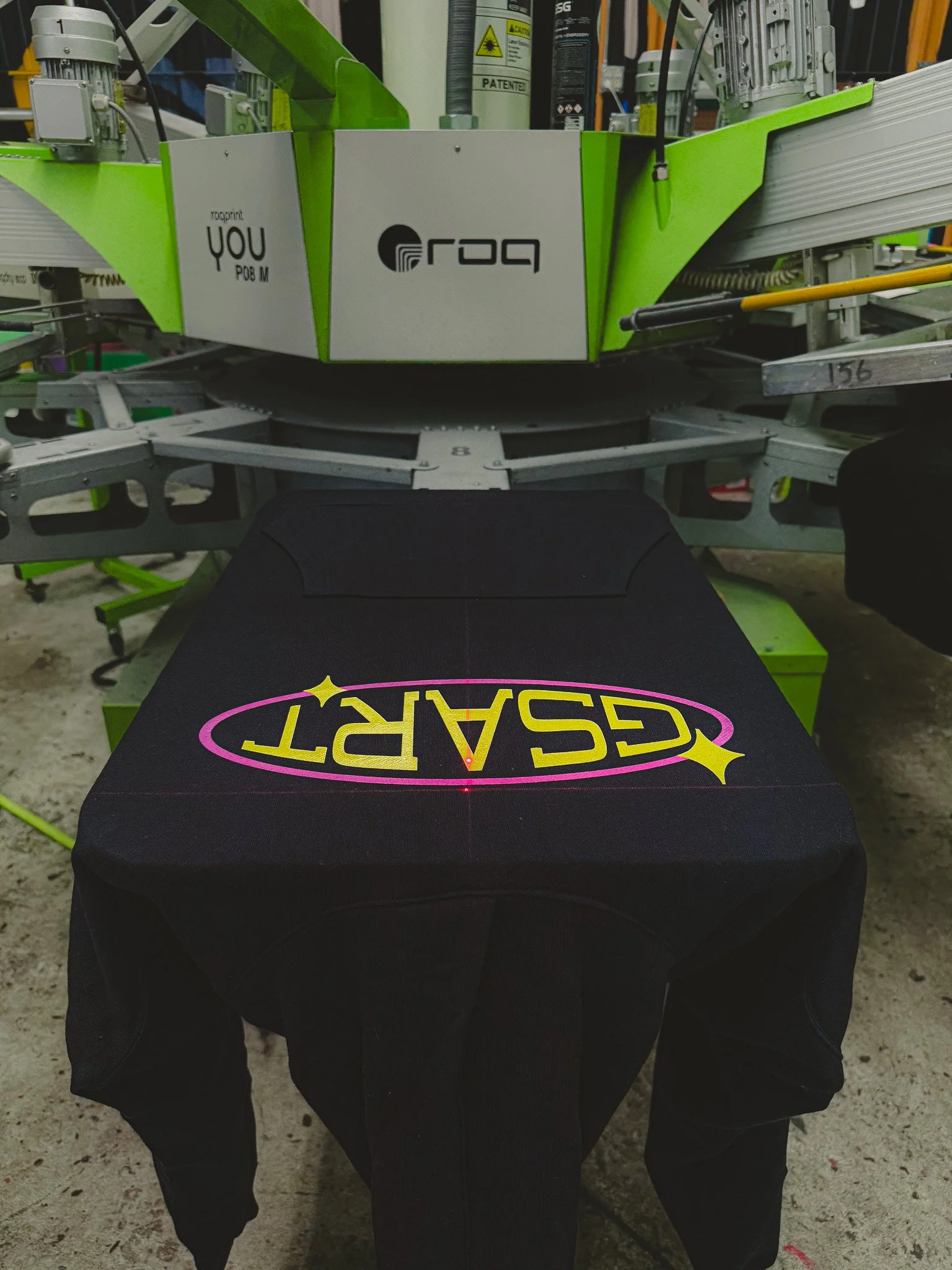 A large industrial printing machine printing the word 'GSPART' on a black fabric material, which is part of a garment or uniform.