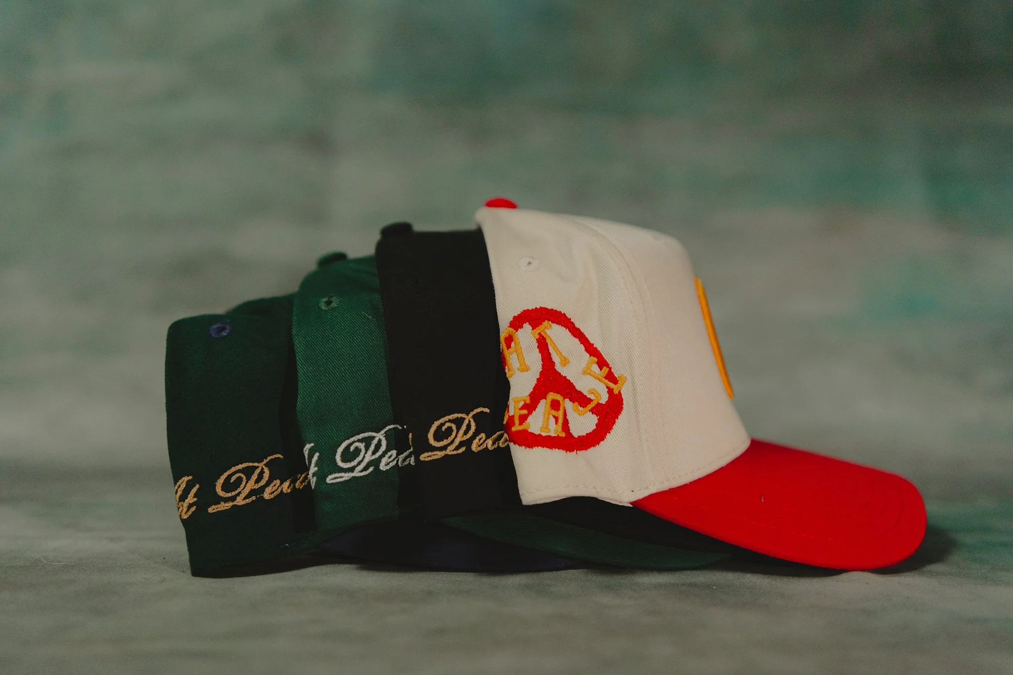 A stack of four baseball caps with various colors and designs, including one with an American flag motif and a red bill, placed on a neutral surface.