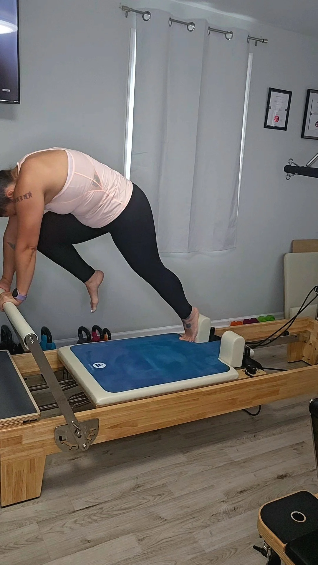 A woman doing reformer Pilates exercises on a wooden reformer machine in a studio.
