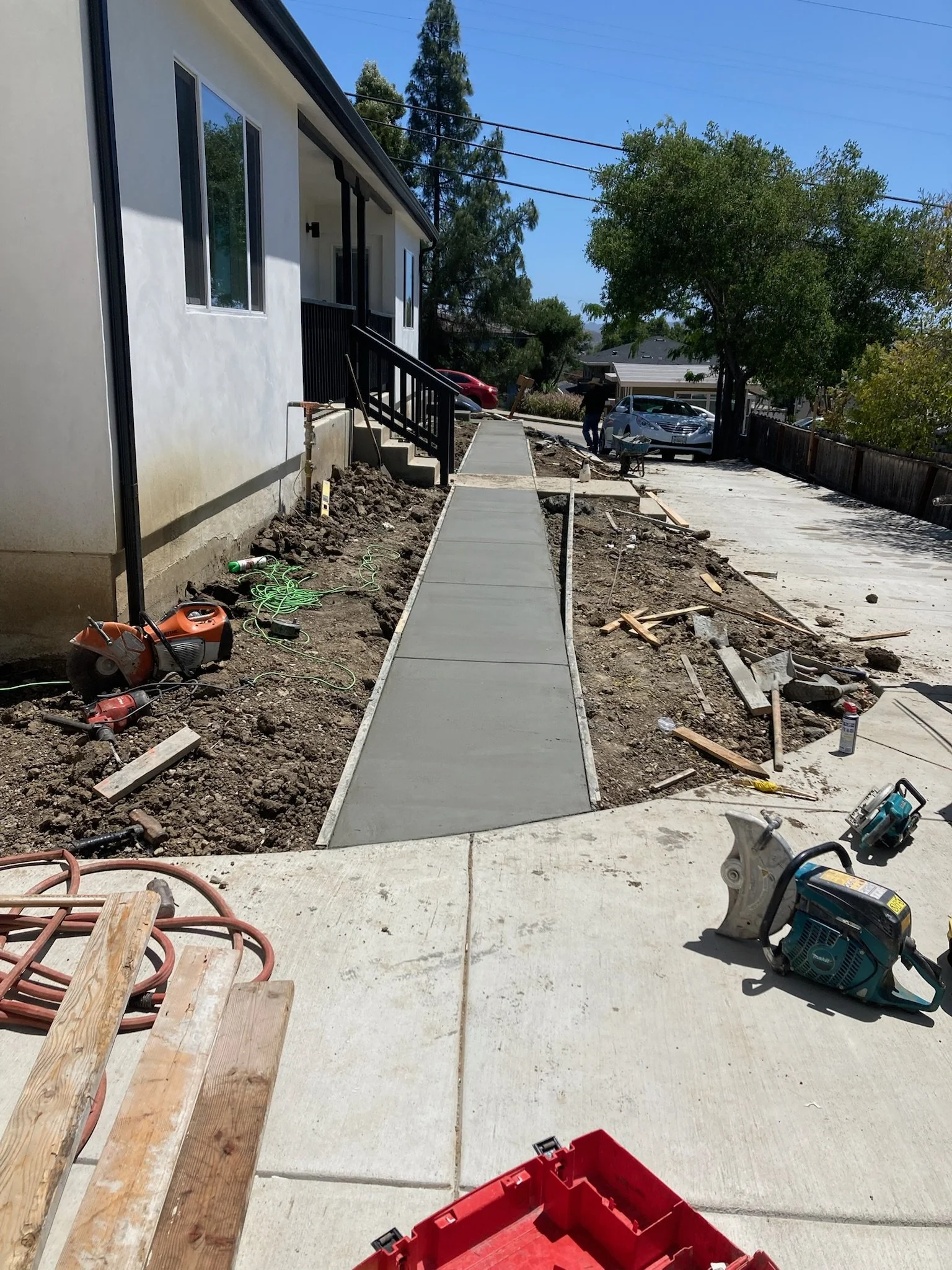 Newly poured concrete sidewalk under construction next to a house, with construction tools and materials scattered around.