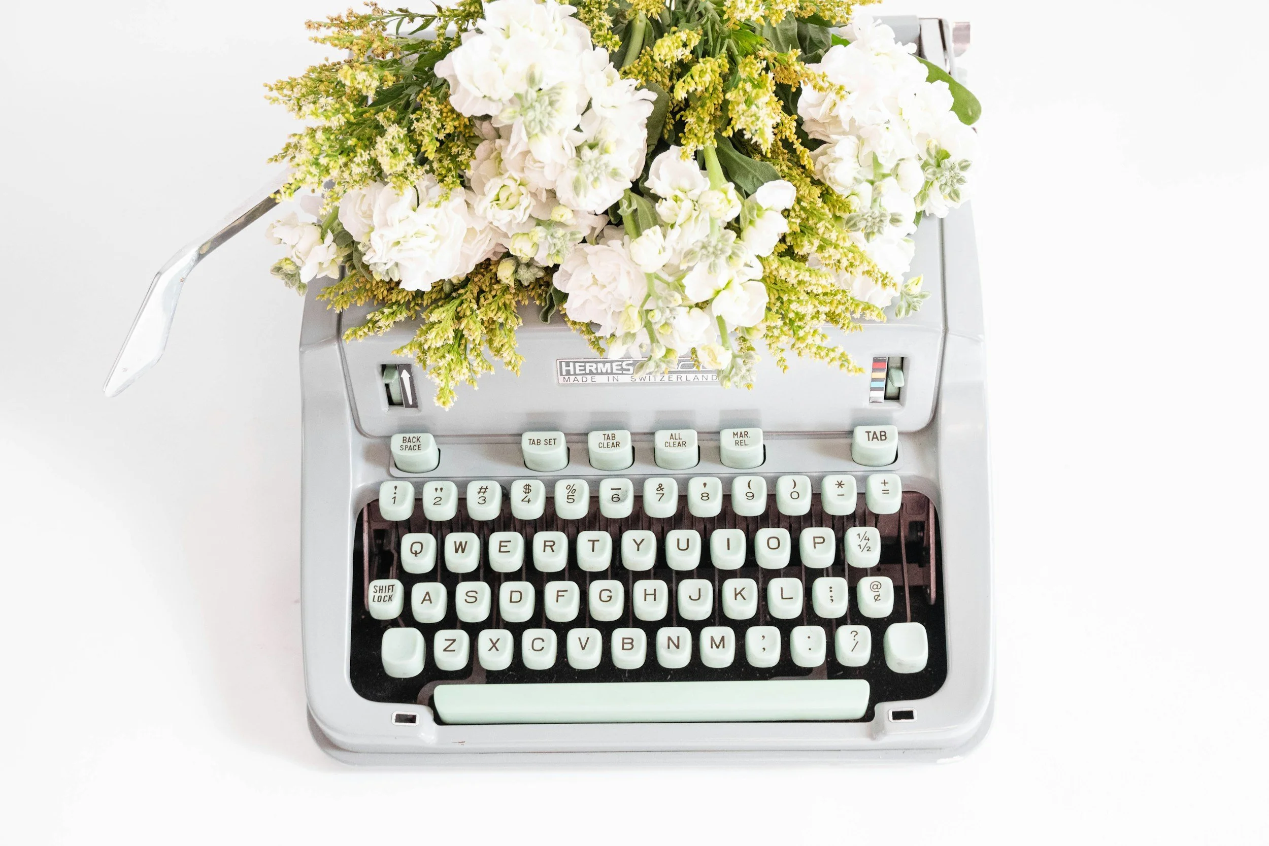A vintage Hermes typewriter with fresh white and yellow flowers arranged on top.