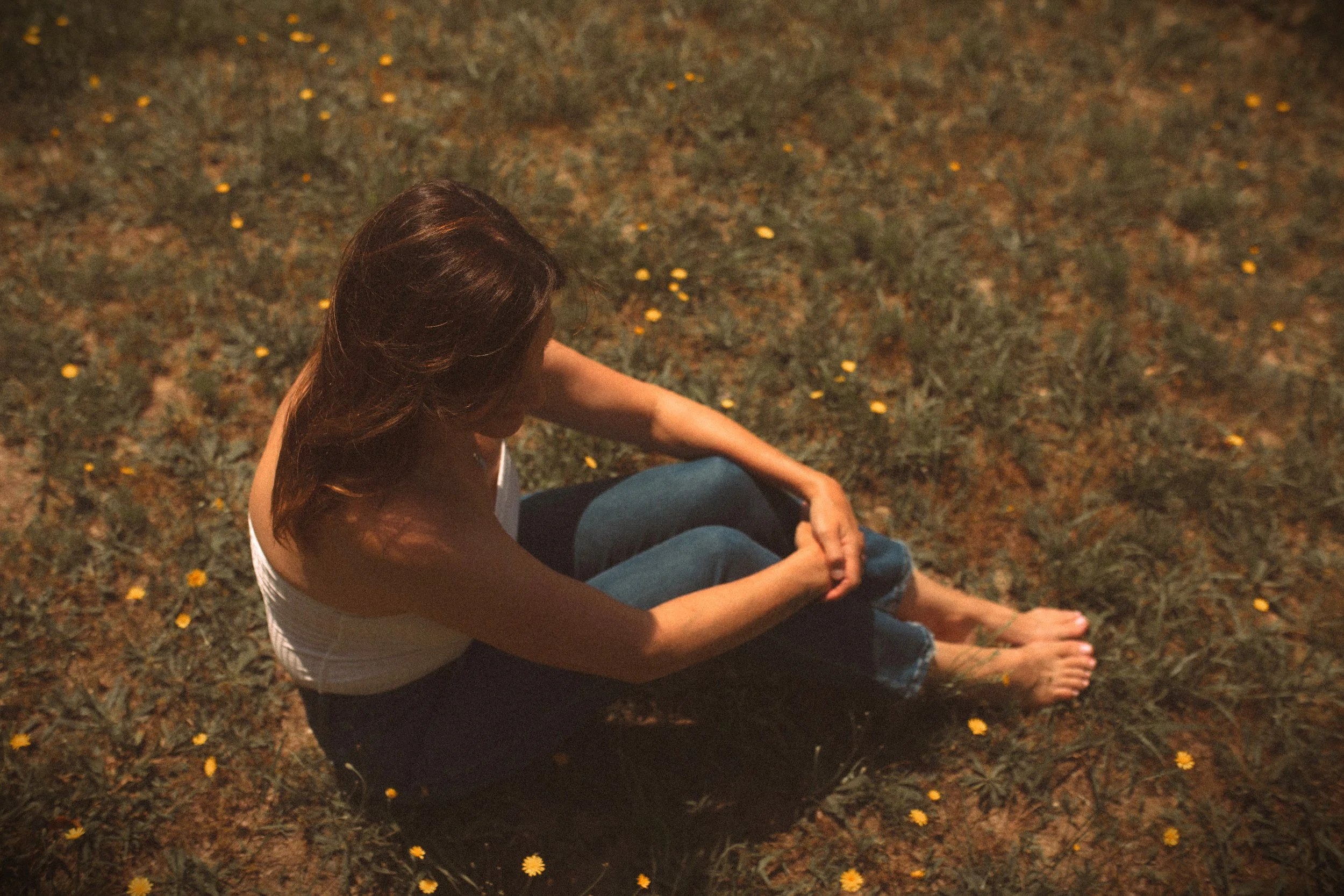 A woman sitting on the ground outdoors at night, with small yellow flowers scattered around her.