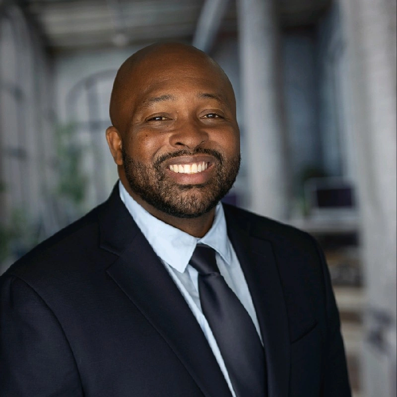 Portrait of a smiling Black man in a suit and tie in an office setting.